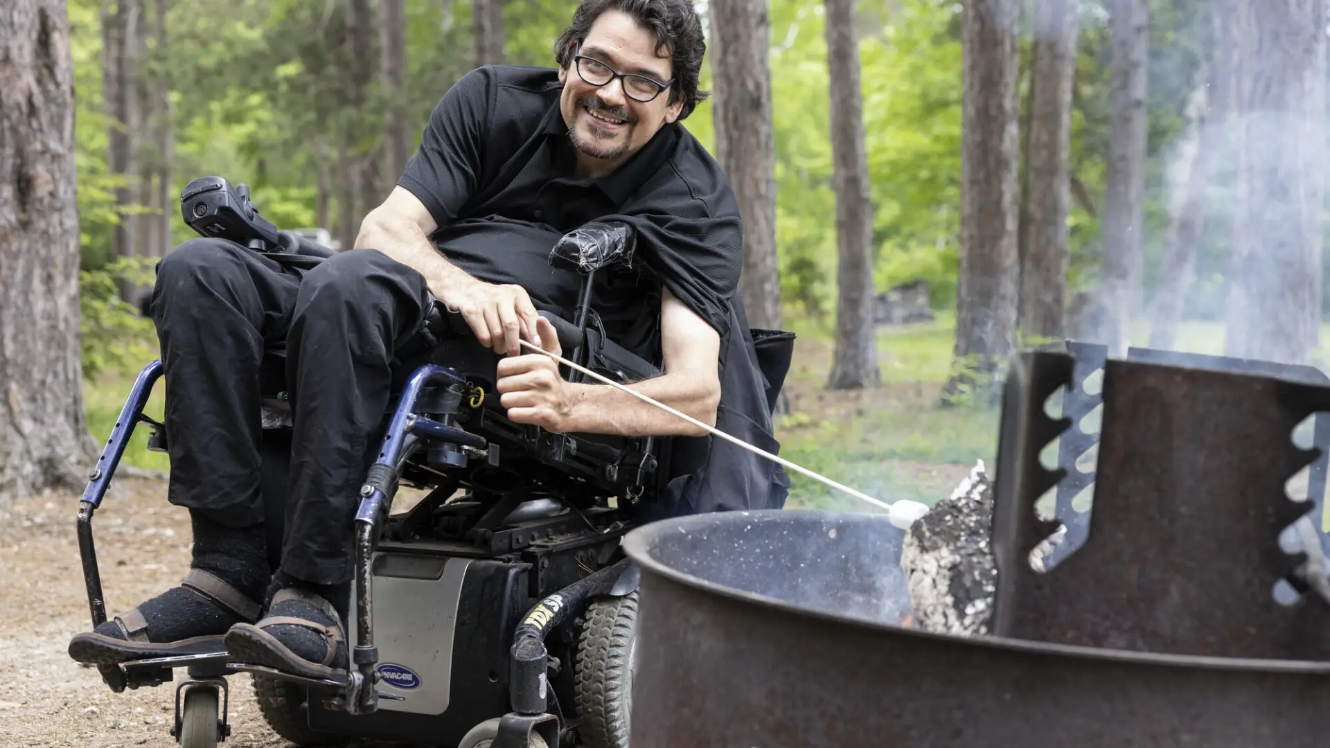 A man in a wheelchairs toasts a marshmallow.