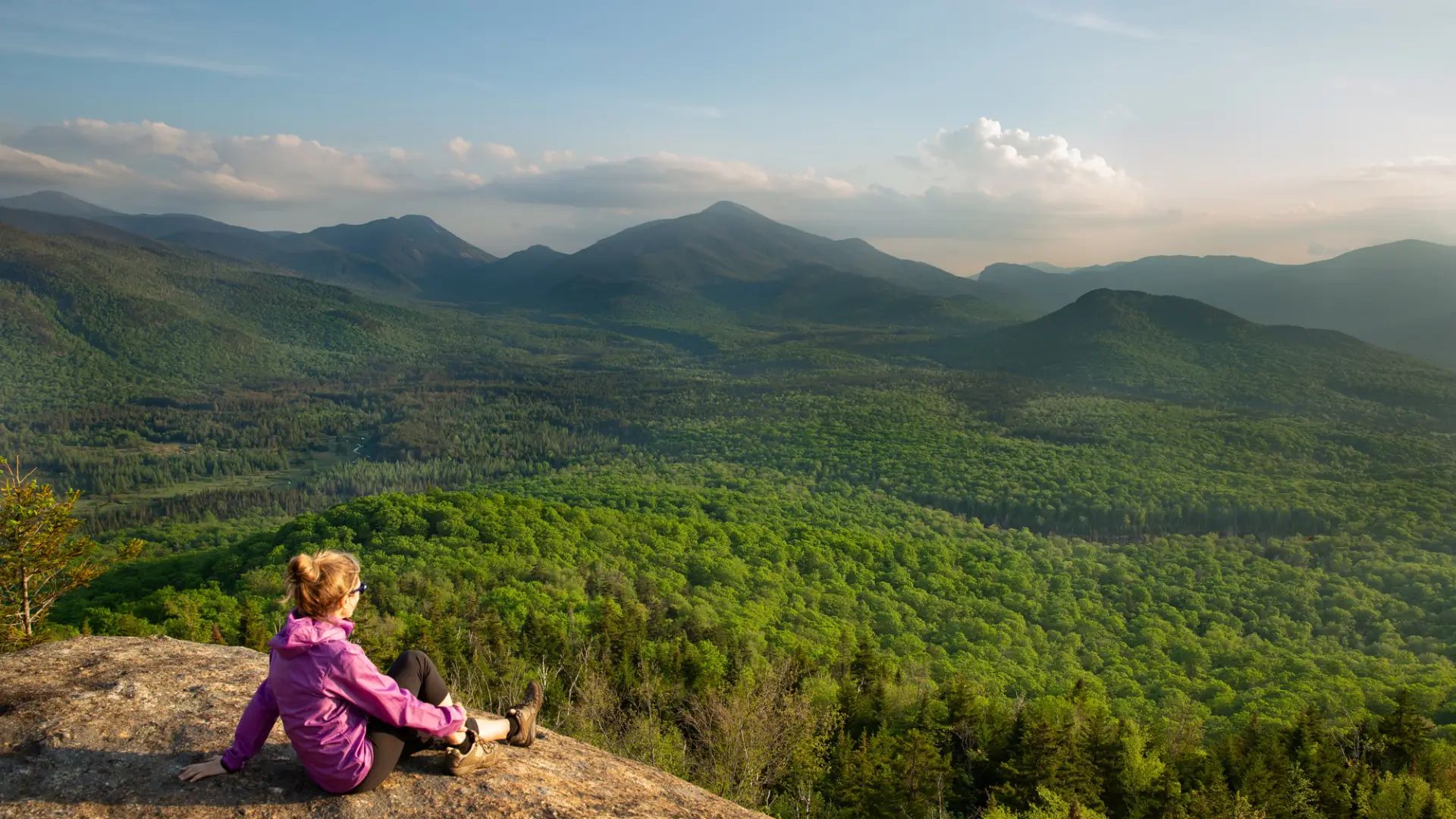 A hiker sits atop a rock, overlooking the mountain range.