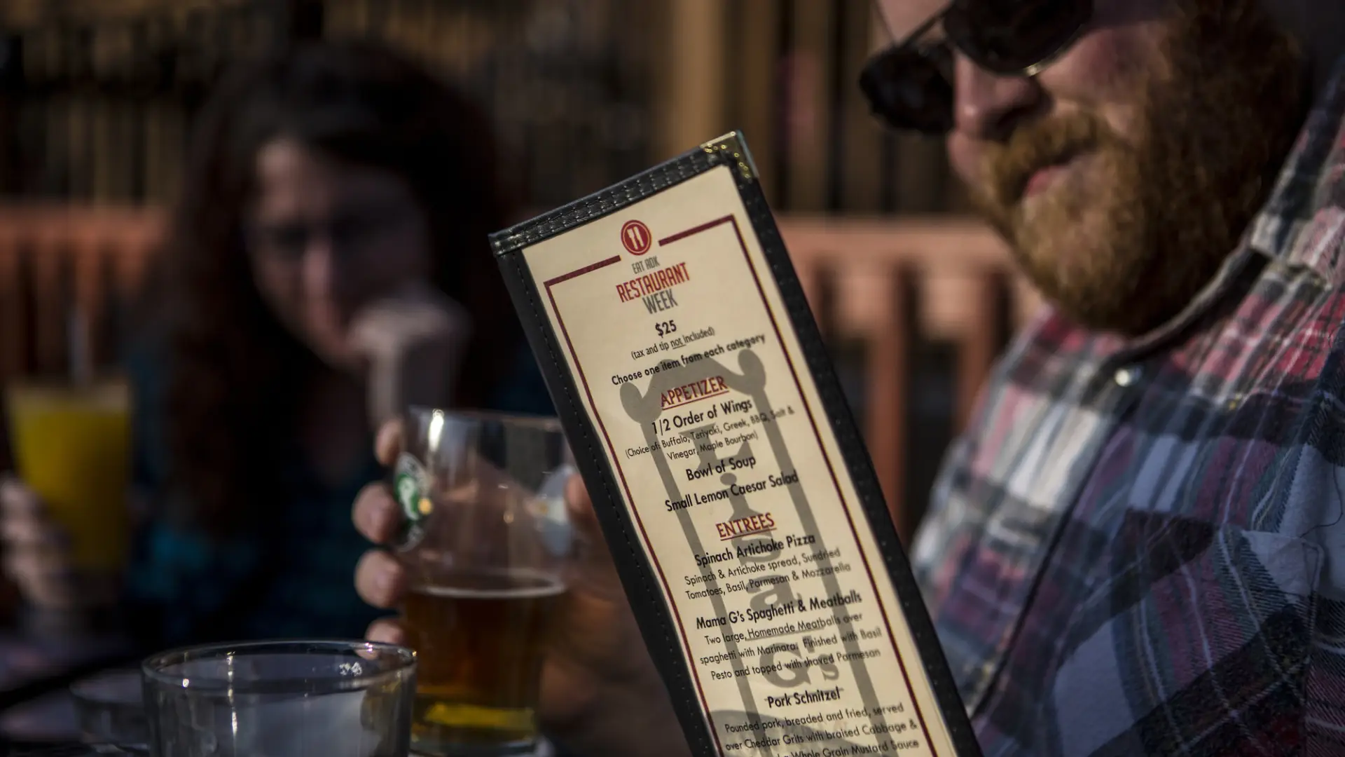 Man looks at menu with drink in his other hand