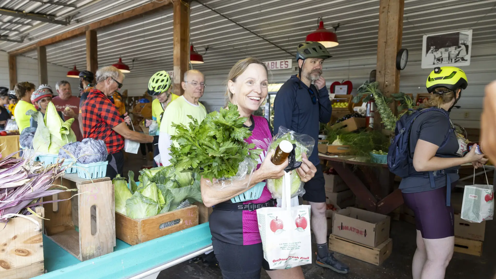 A group of people walk through a farmers market with produce in their hands. 
