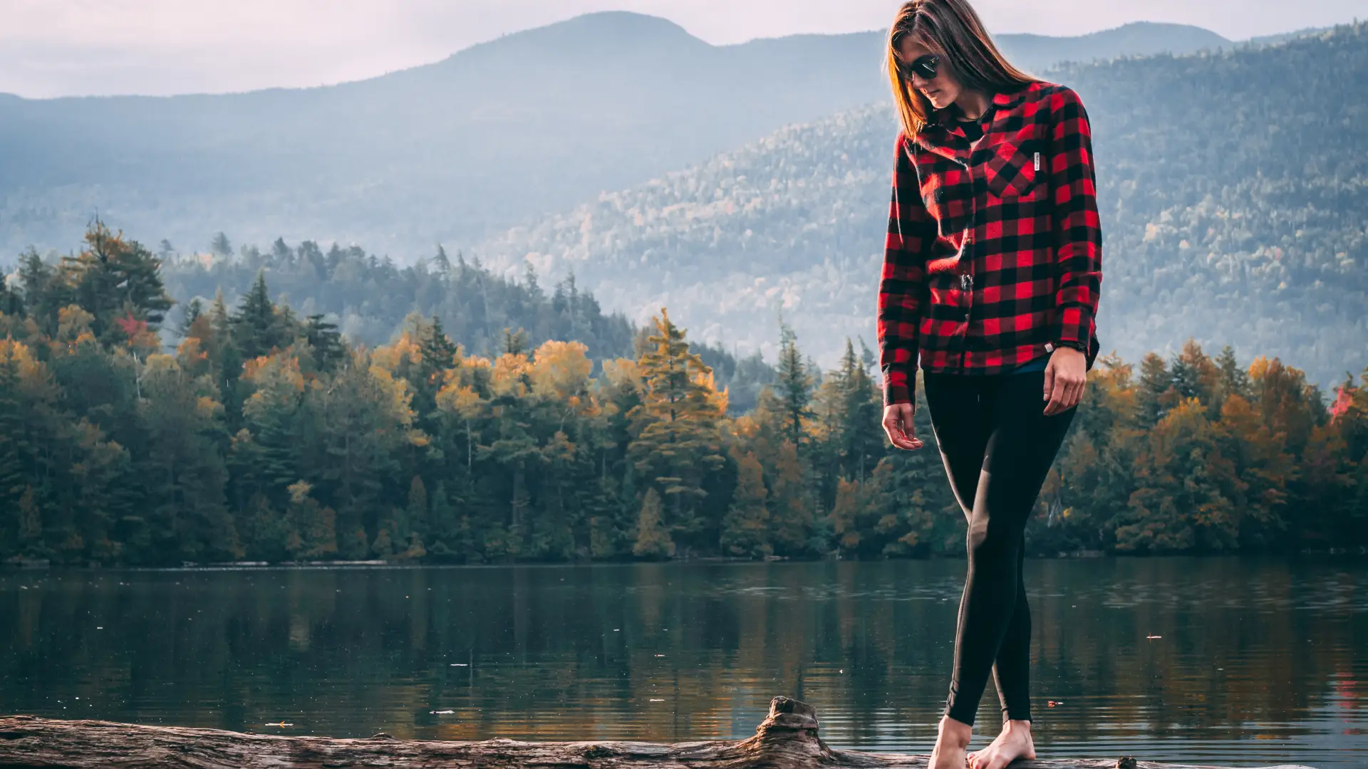 A woman walks on a log in a pond