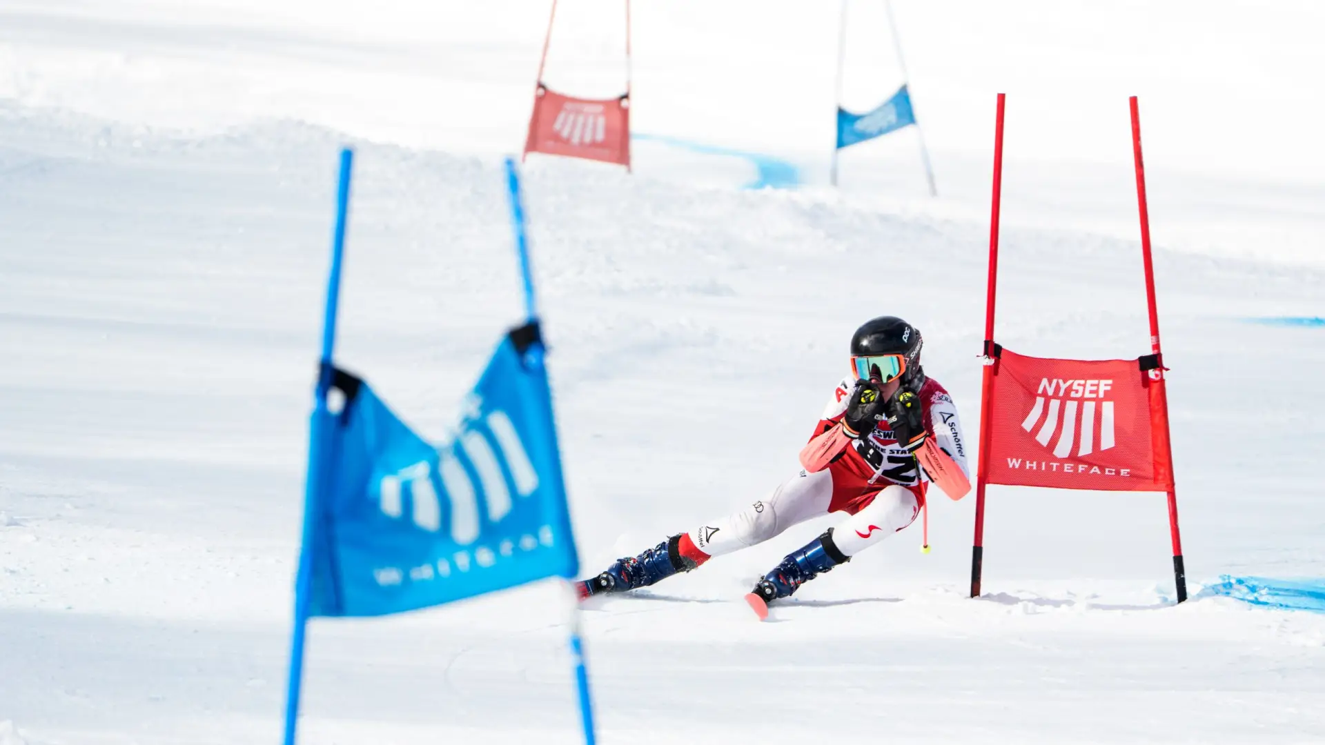 A young skier in action, racing past blue and red flags at Whiteface Mountain ski resort, showcasing agility and skill on fresh snow.