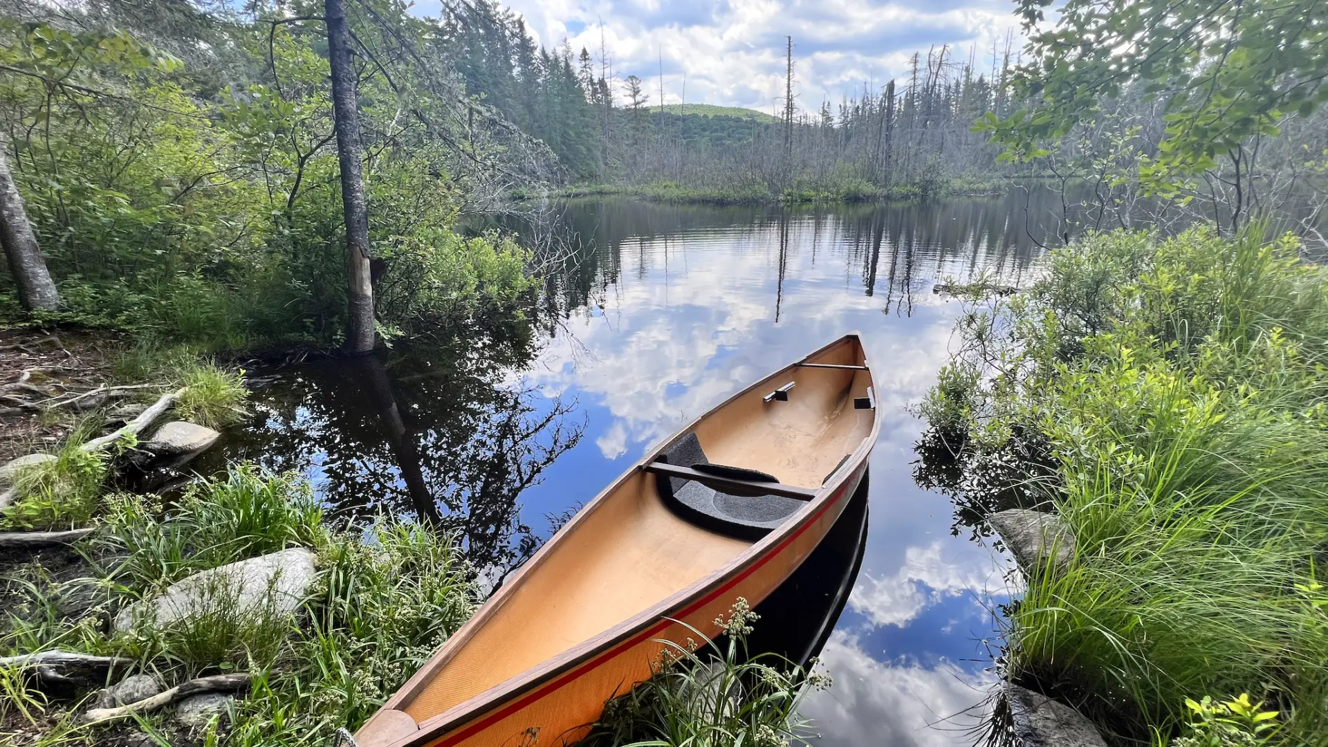 A light brown lightweight canoe at a launch on a backcountry river.