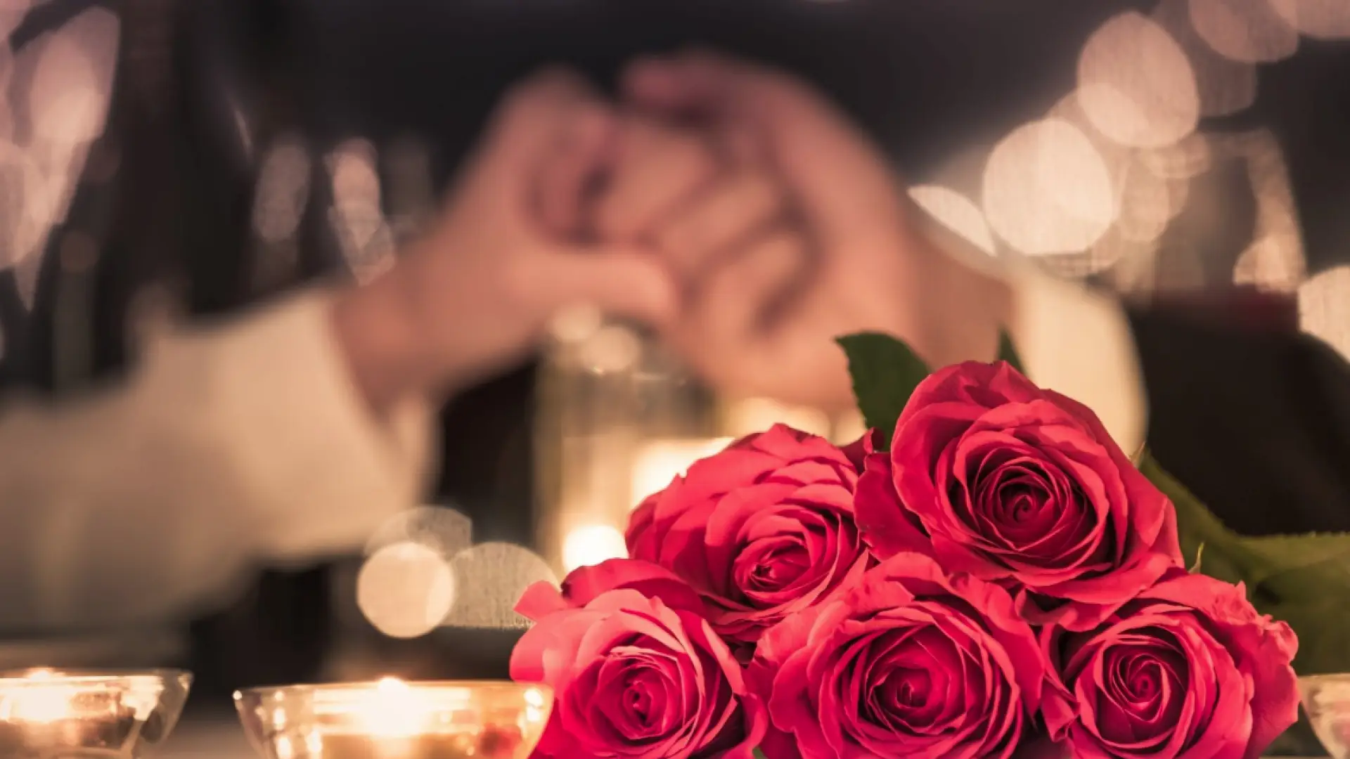 Bunch of roses on candlelit table with people holding hands