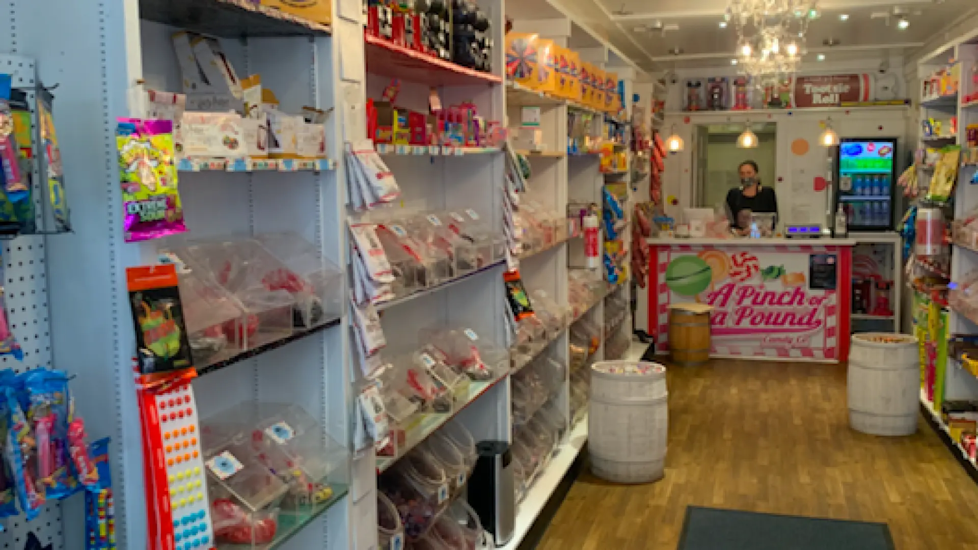 A white shop with chandeliers and shelves filled with brightly colored candy.