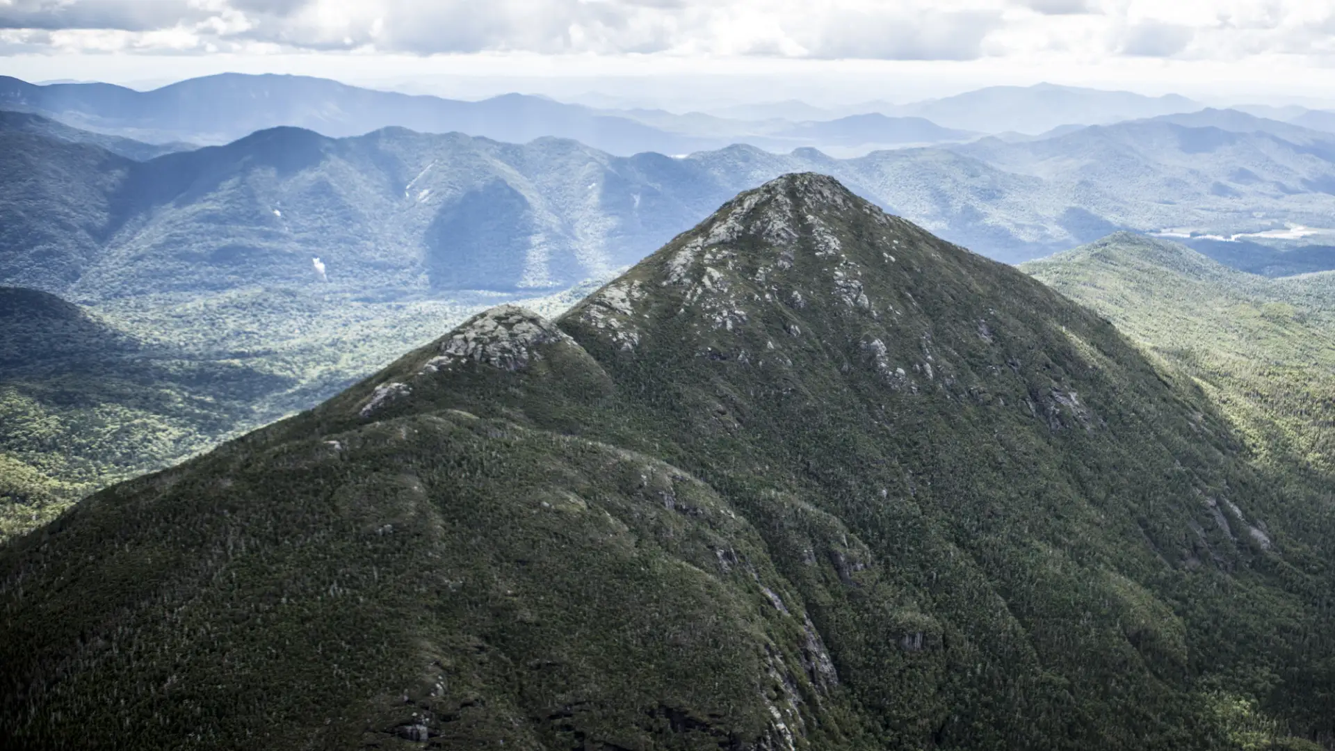 An aerial view of the towering High Peaks, with rocky summits and forested slopes.