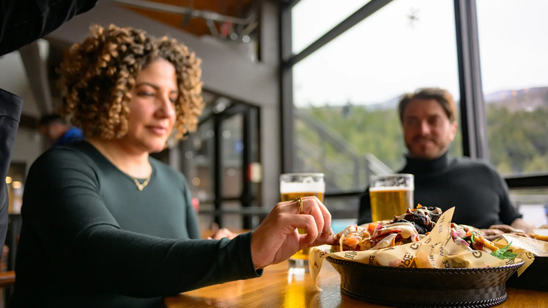 A woman with very curly hair takes a bite from nachos.