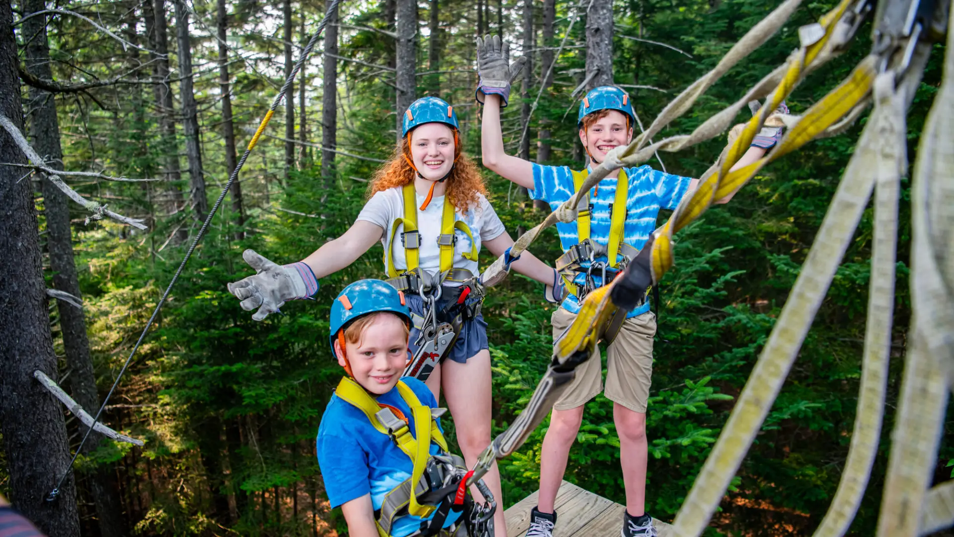 Three children smiling and geared up to go, posing for a picture at the zipline.