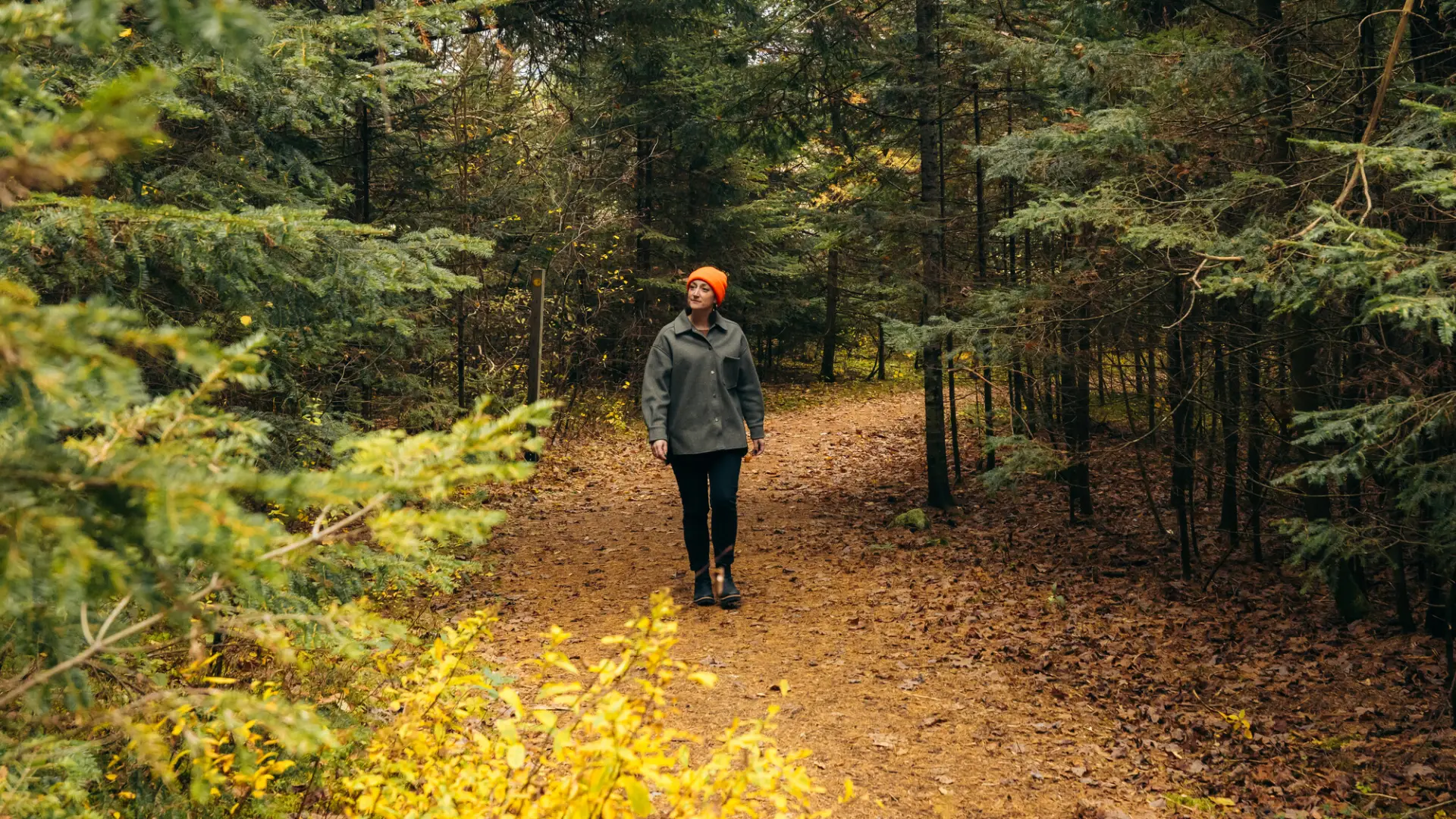 A woman standing on a trail during the fall with a bright orange hat on.