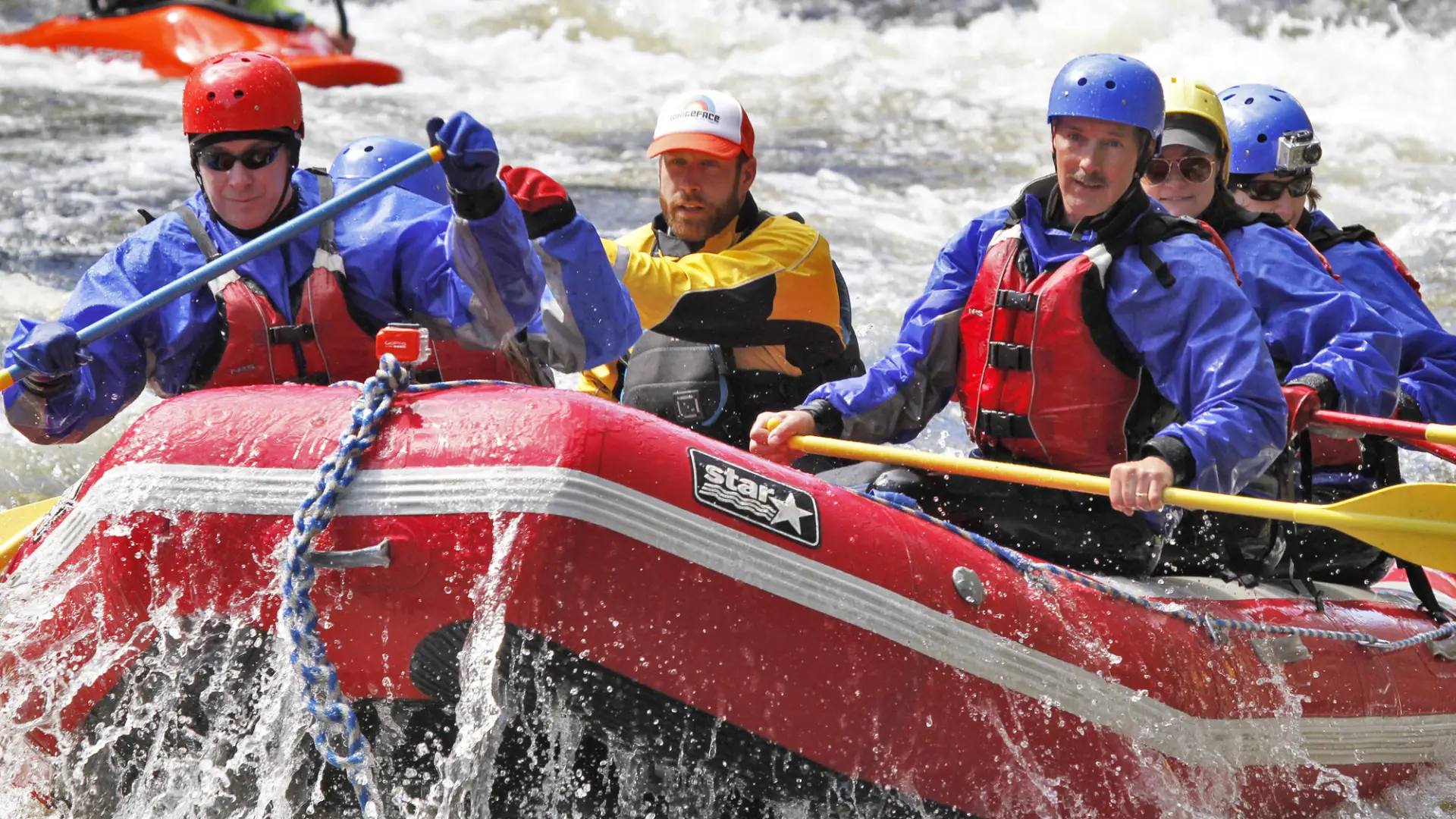 A group of people wear rafting gear and paddle through rapids.