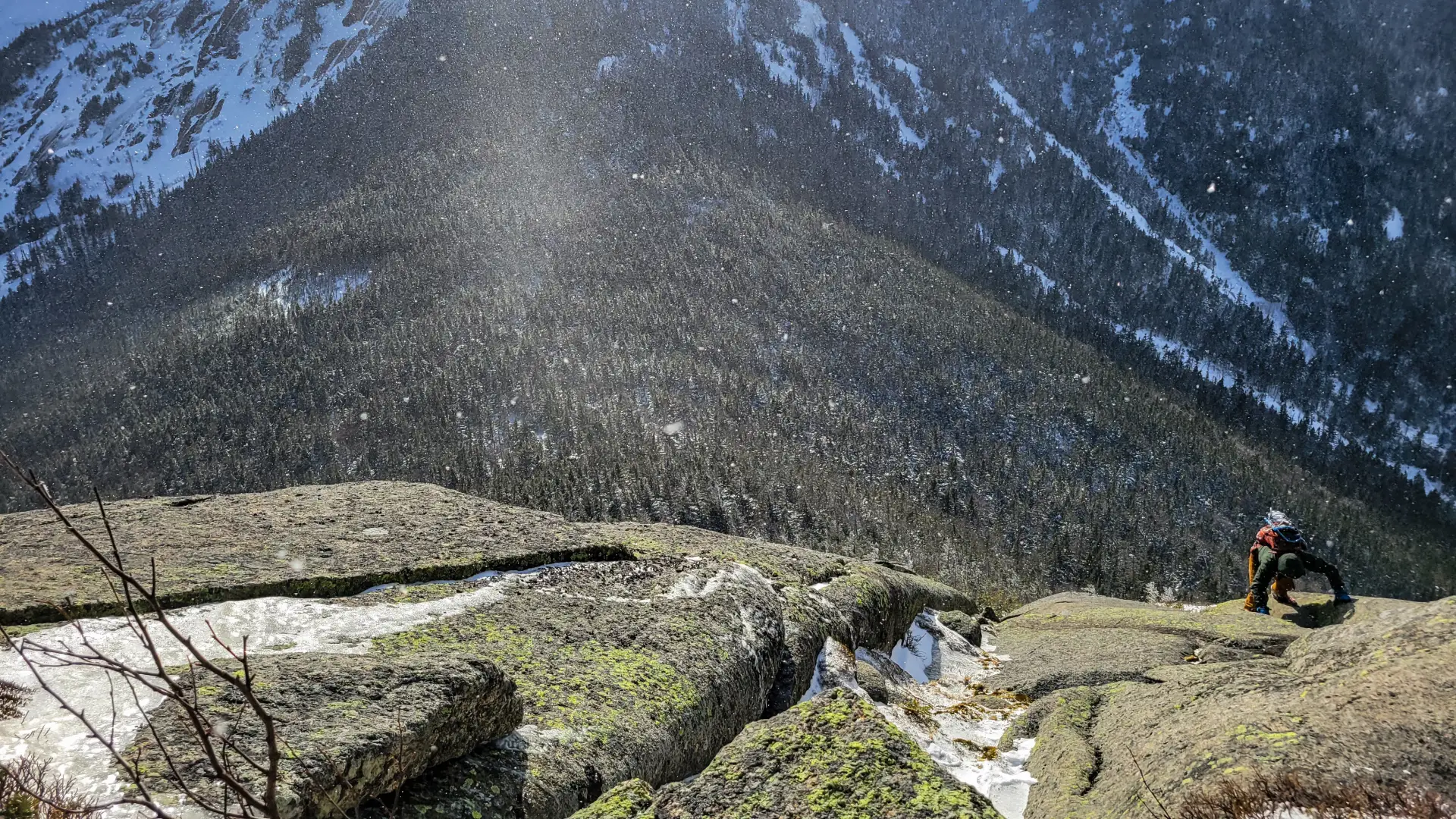 A hiker making his way up a rock slab in the winter mountains.