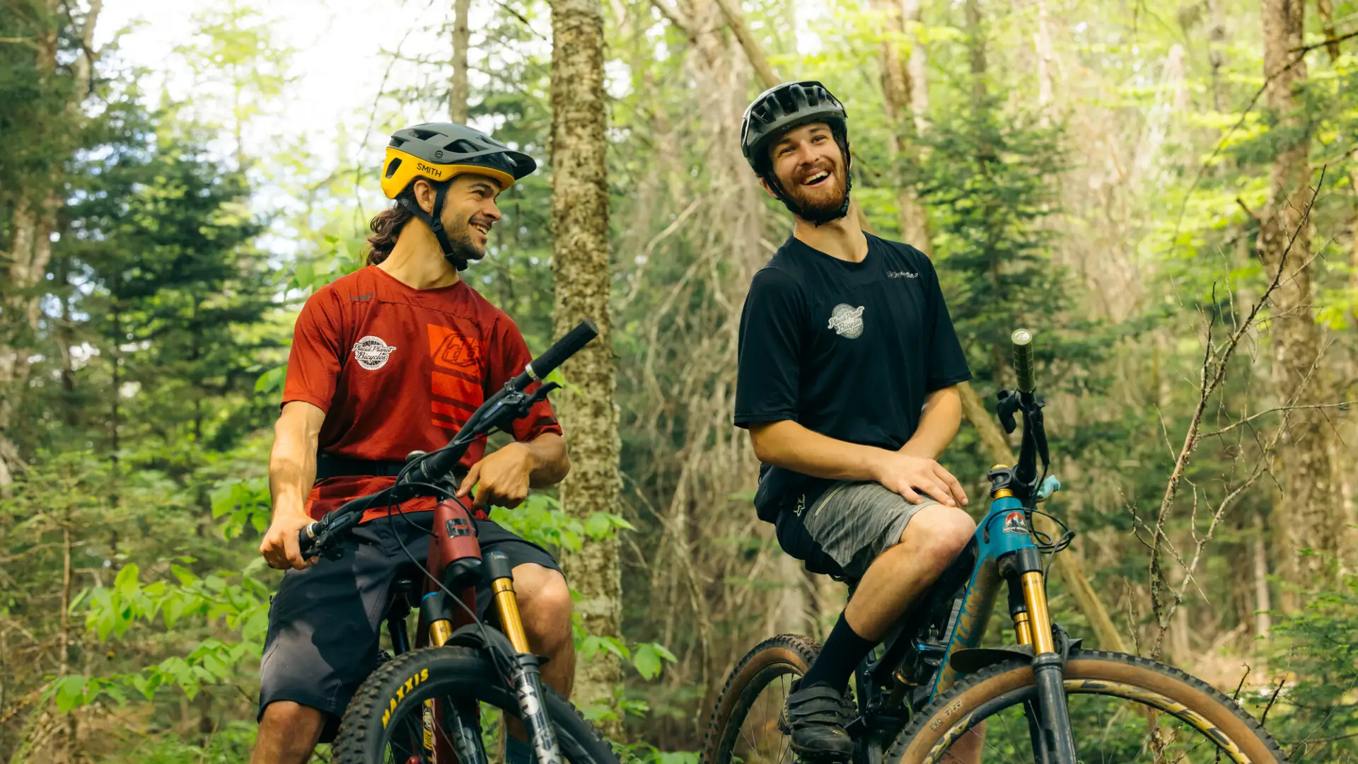 Two bikers on a trail standing and laughing together.