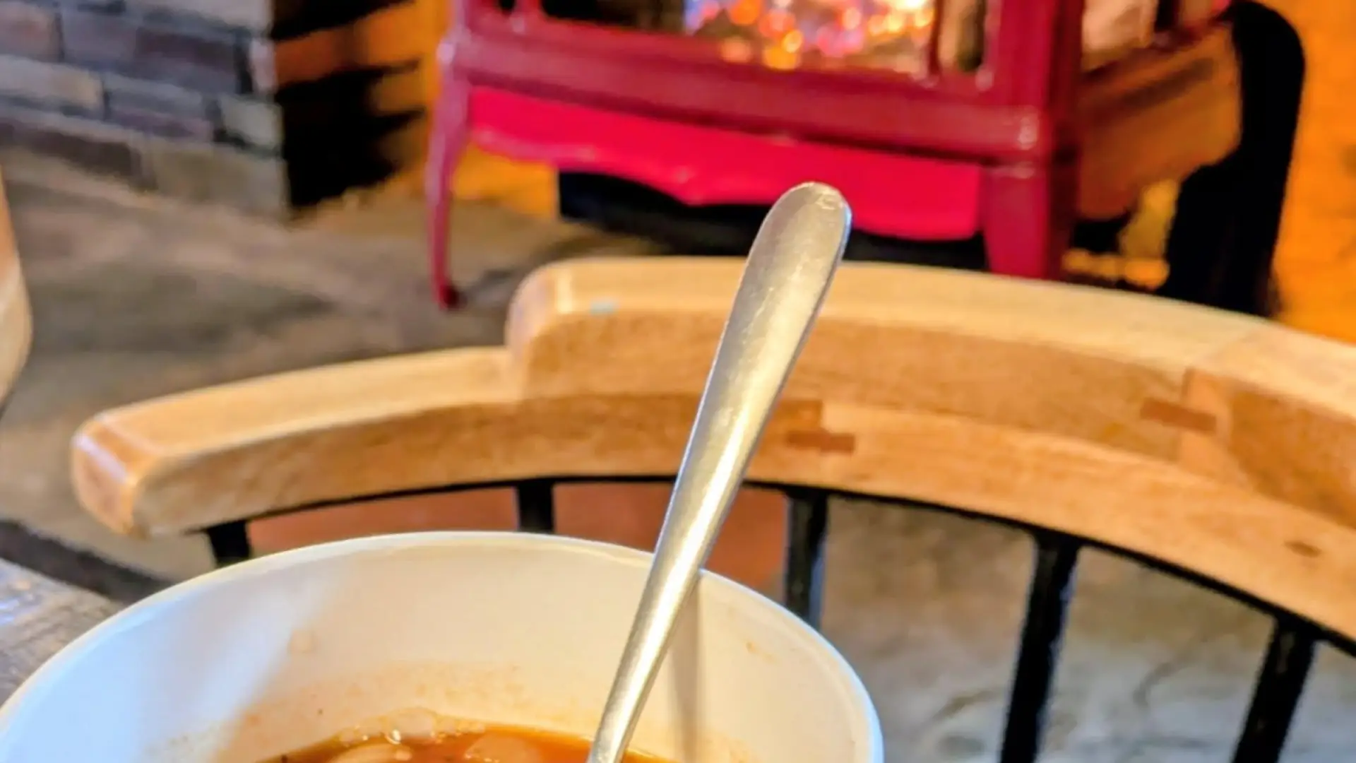 A cup of rich soup next to the red gas fireplace