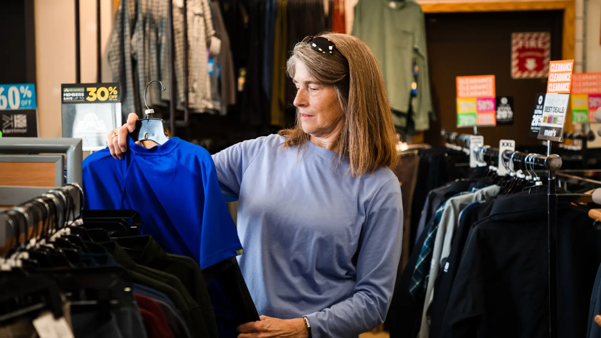 A woman contemplates buying a blue t shirt in a store.
