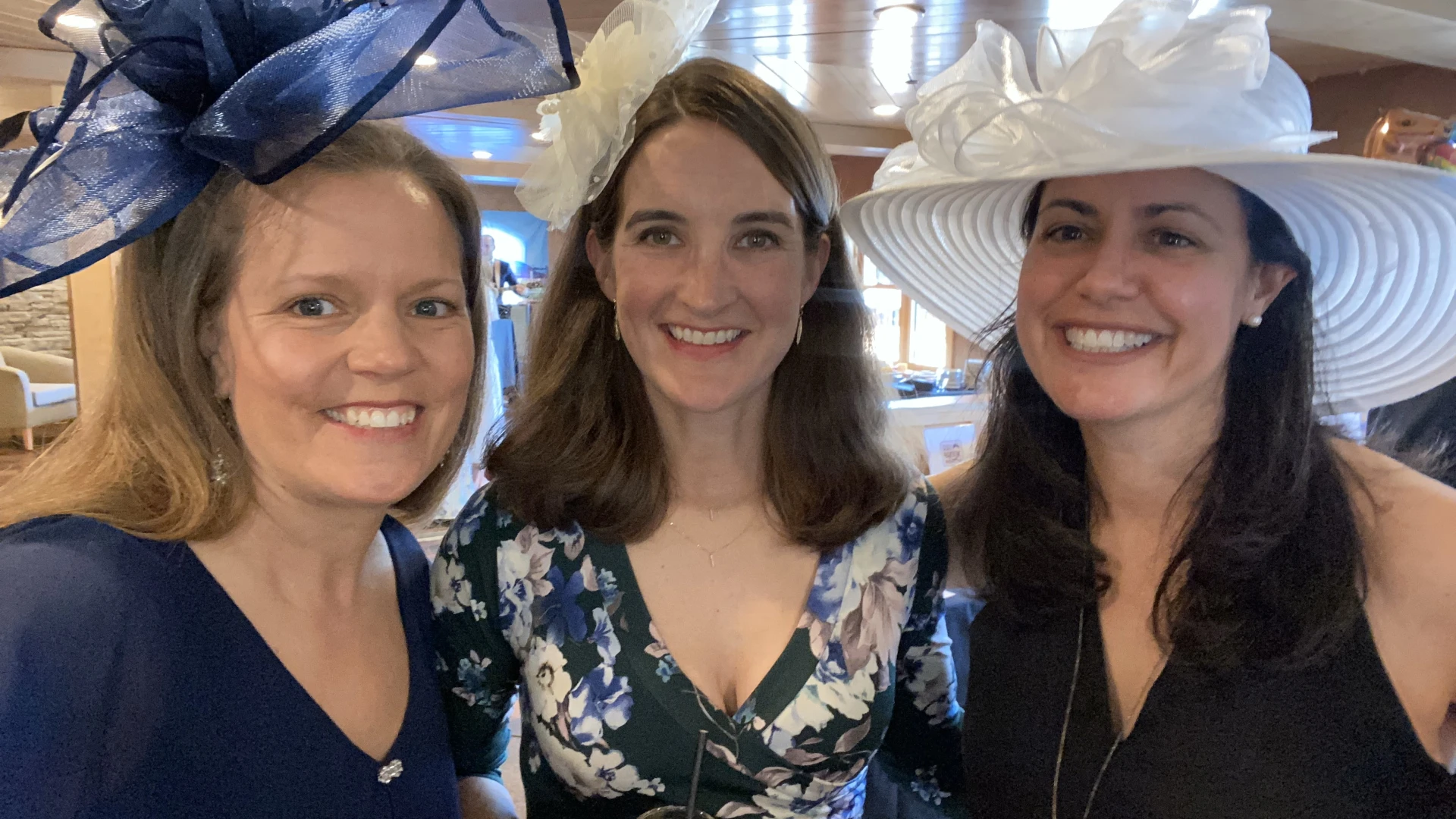 Three women in Kentucky Derby dress and hats smile together for the camera