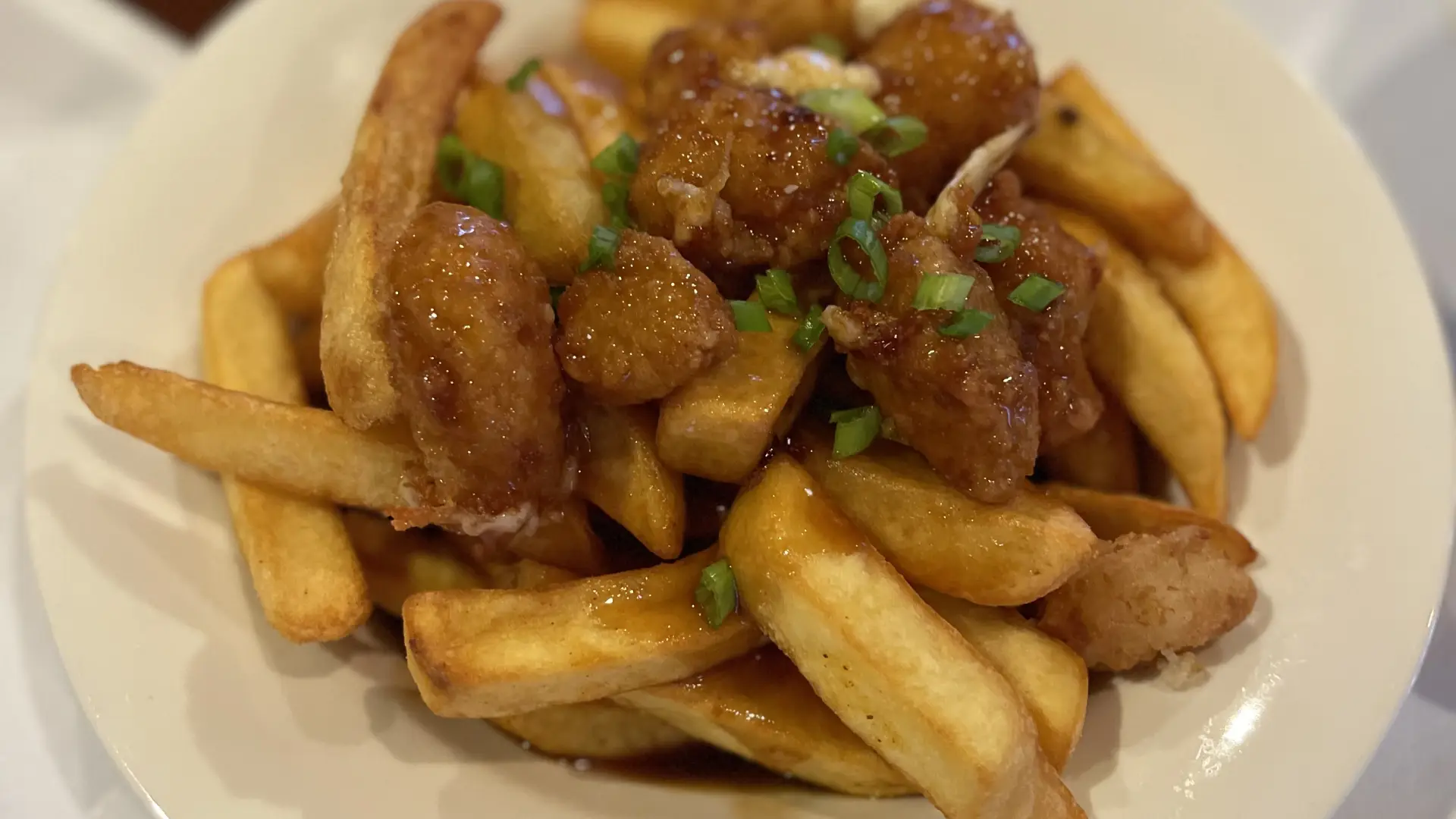 Extreme close-up of a dish of glazed, fried cheese curds on a bed of French fries.