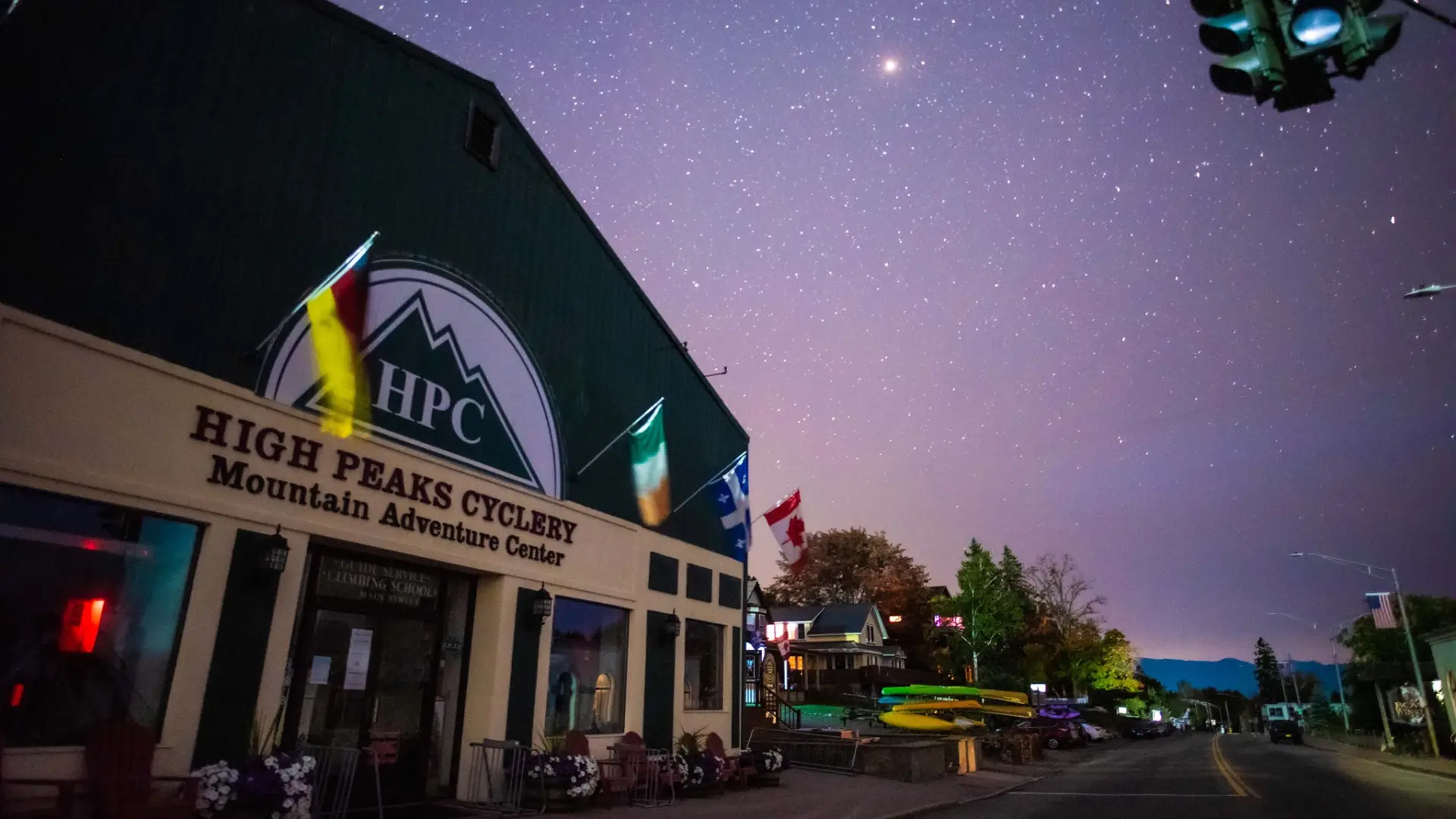 The storefront of High Peaks Cyclery Mountain Adventure Center at night, with a clear shy and bright stars in the sky