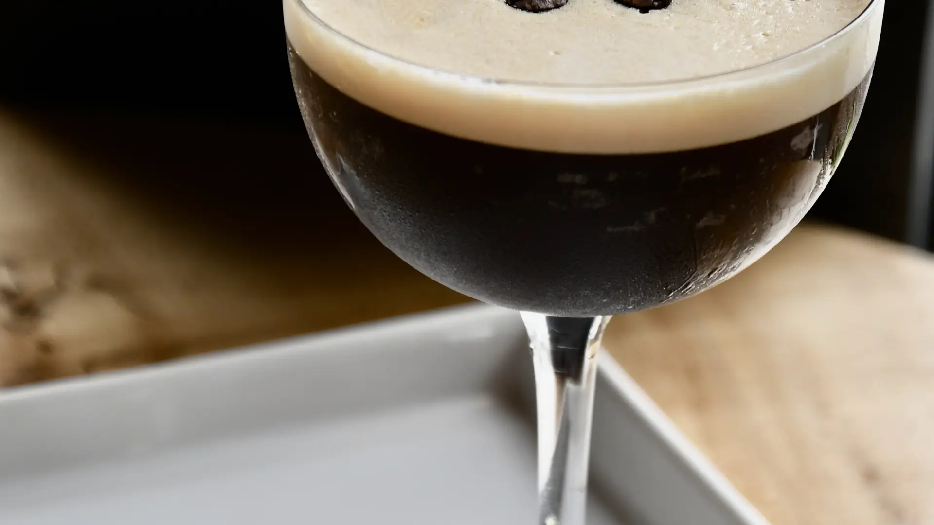 Espresso martini in a coup glass on a white plate scattered with coffee beans