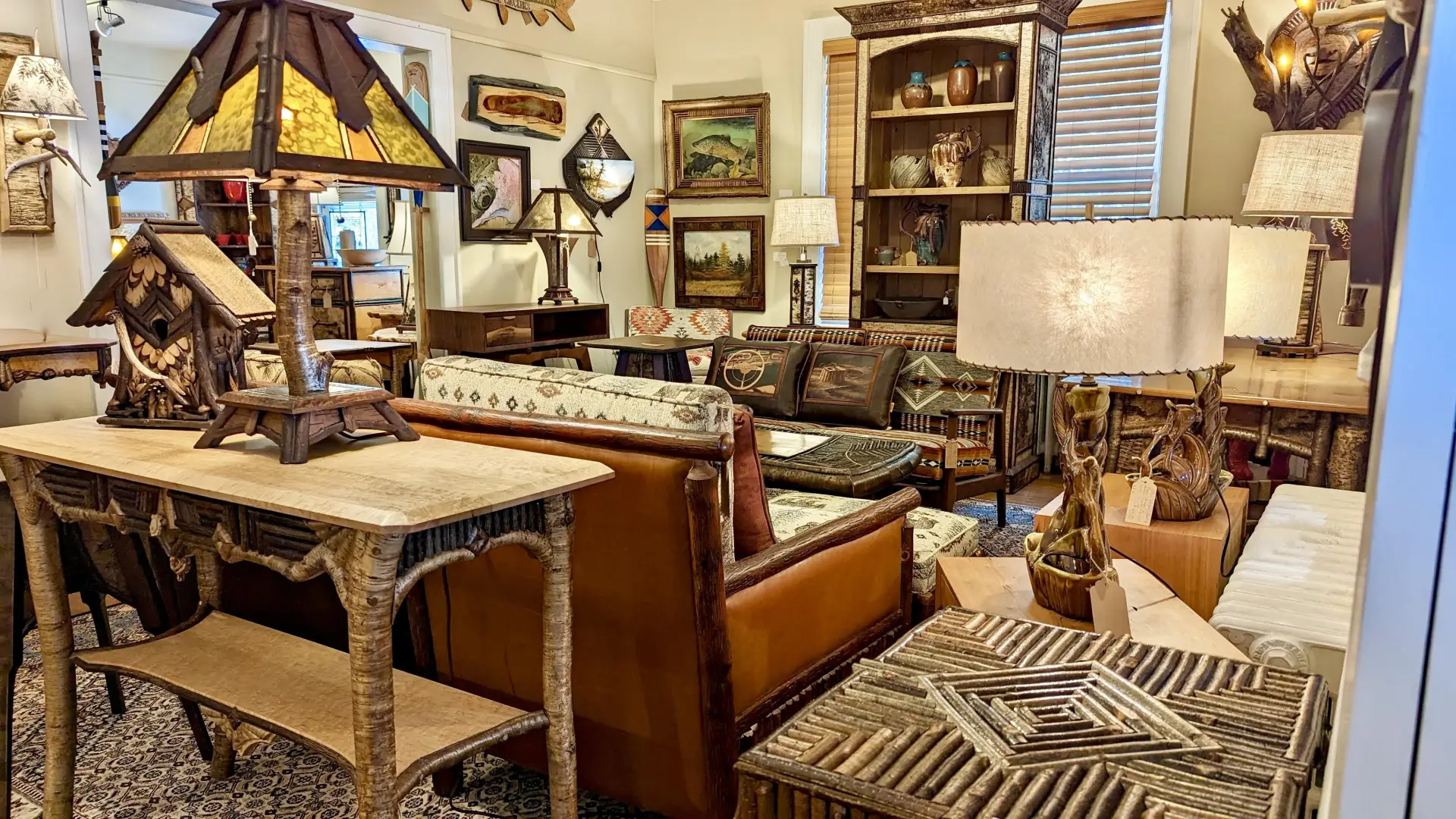 A view of the show room at L Post Rustics featuring many styles of log furniture from end table to couches, table lamps, sconces and tall hutches flanked by wall decor.