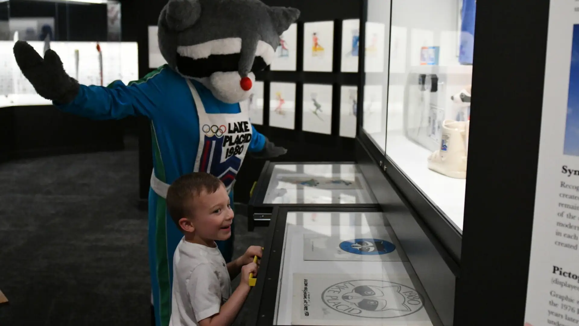 Young boy looks at Olympic Museum display with Roni the Raccoon mascot
