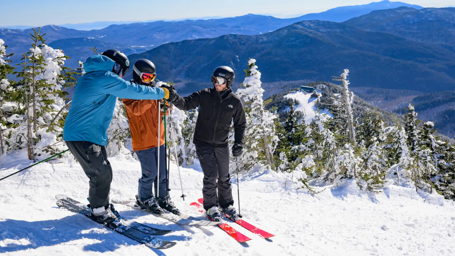A group of skiers smile and take photos on top of a mountain. 