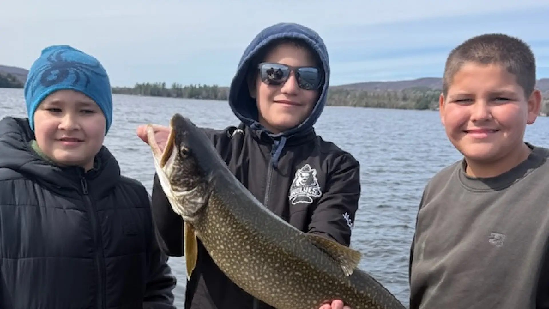 Three kids hold a fish and smile at the camera