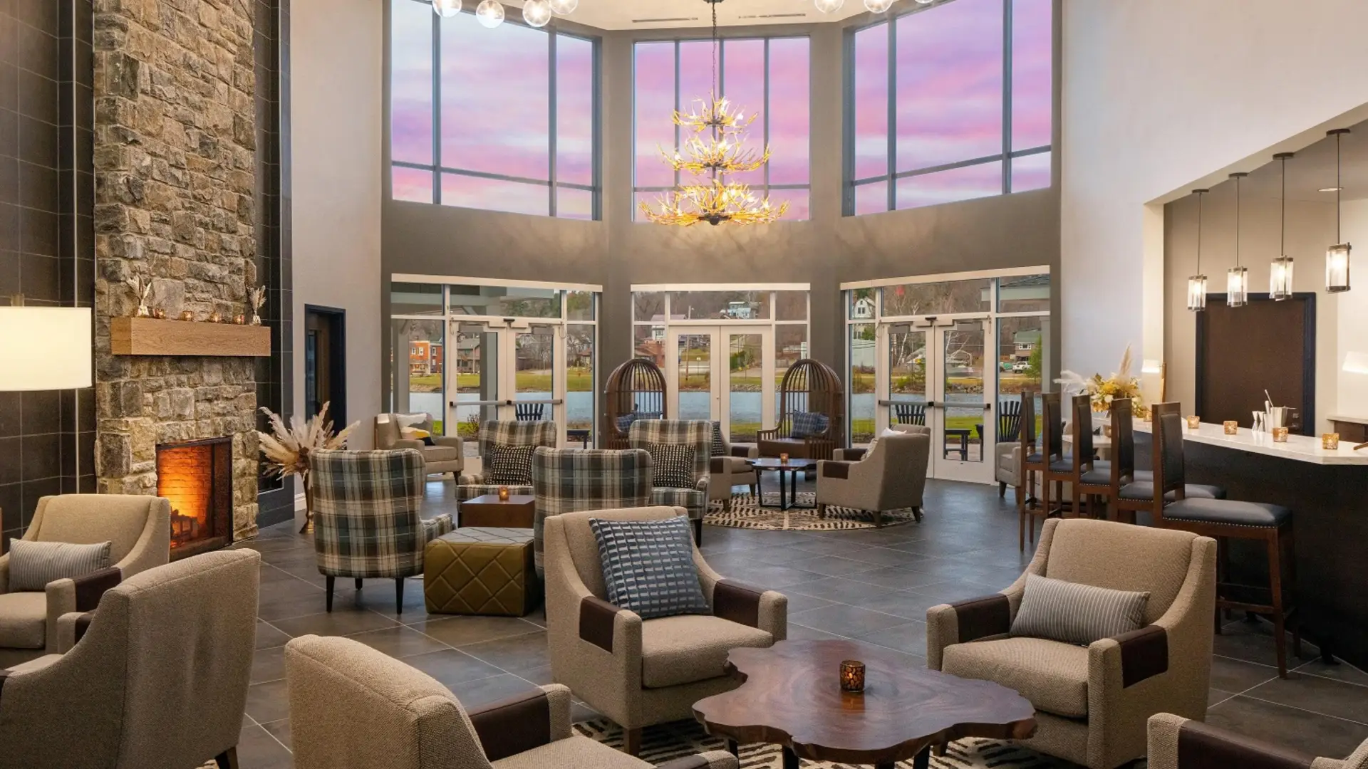 Grand lobby space with stone fireplace, plush armchairs and a view of the lake and mountains