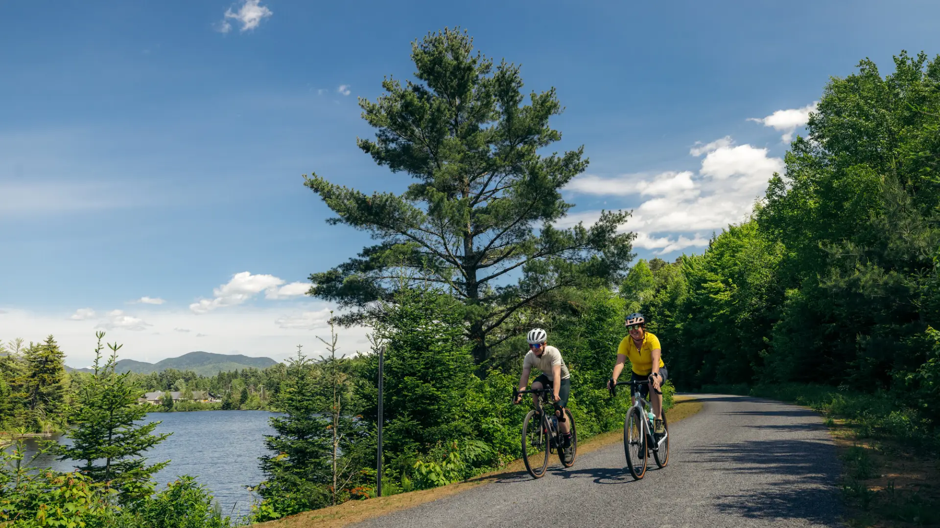 Two people on bicycles ride on rail trail next to trees and water