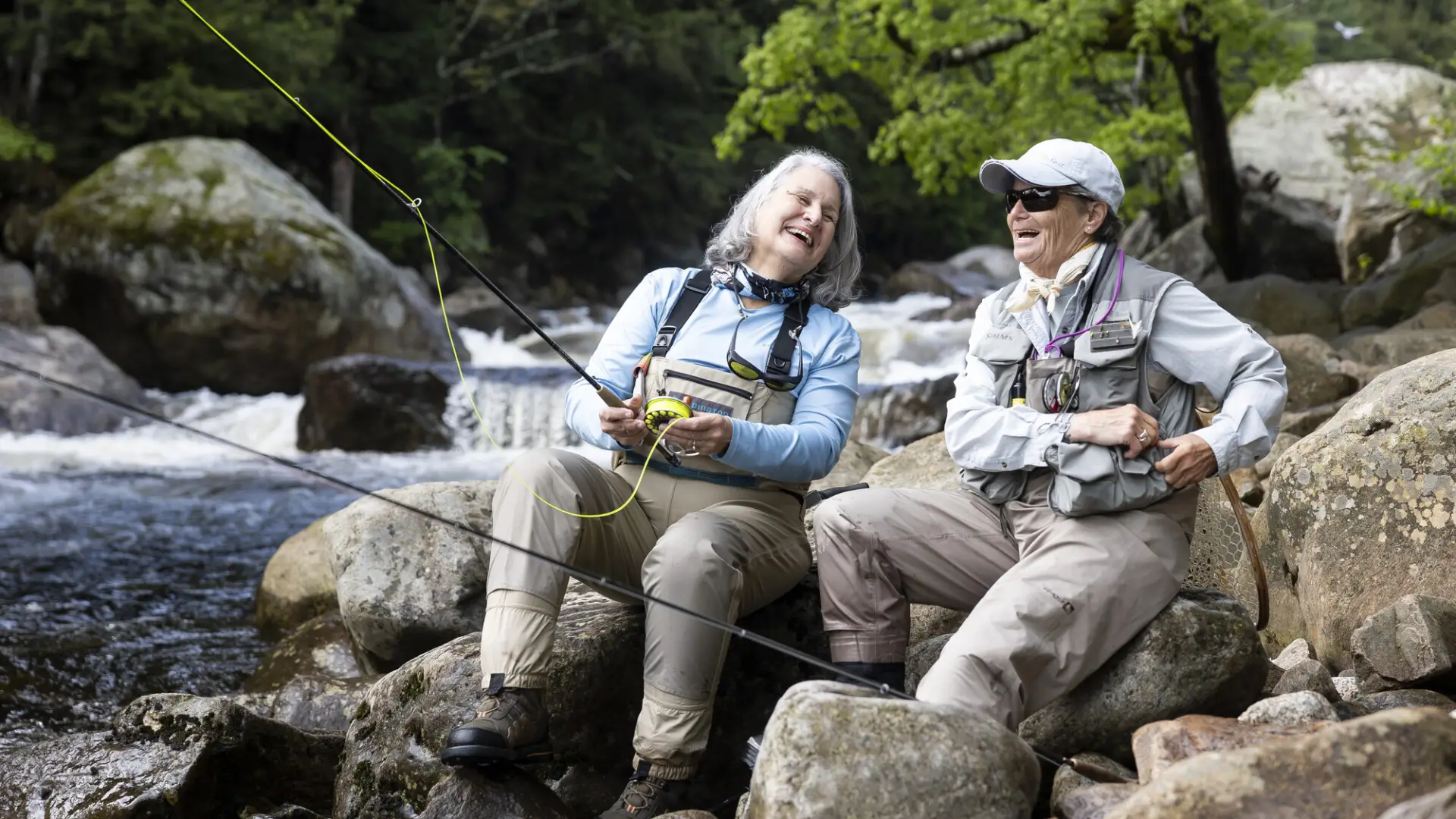 Two fisherwomen laugh on banks of river