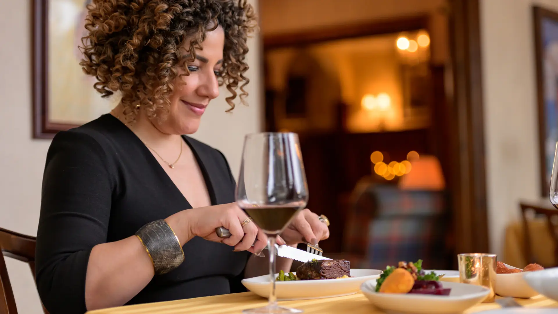 A woman at the Interlaken Inn Restaurant cuts her meal with a glass of wine and warm glow from the fireplace