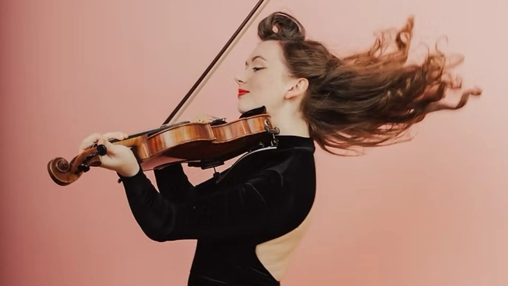 Kathleen Parks in black velvet dress plays fiddle in front of pink background