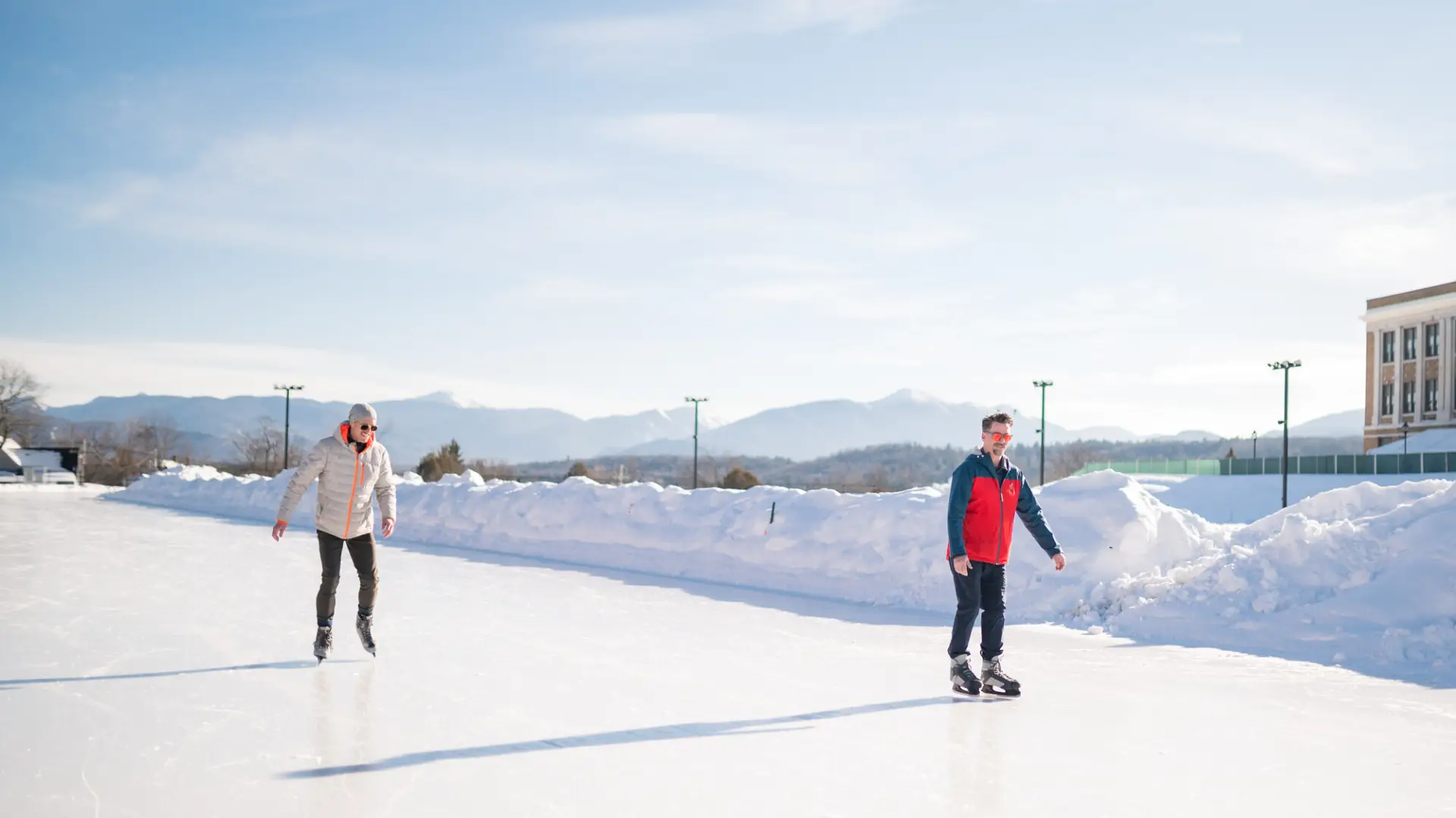 Two men ice skate on Olympic Oval on snowy bluebird day