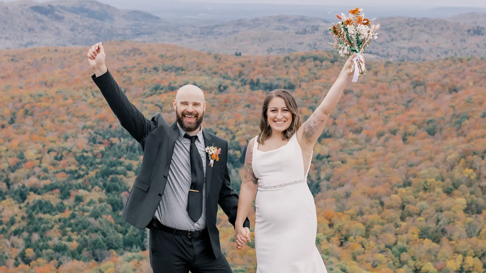 Bride and Groom rejoice and wave arms, smiling at the camera