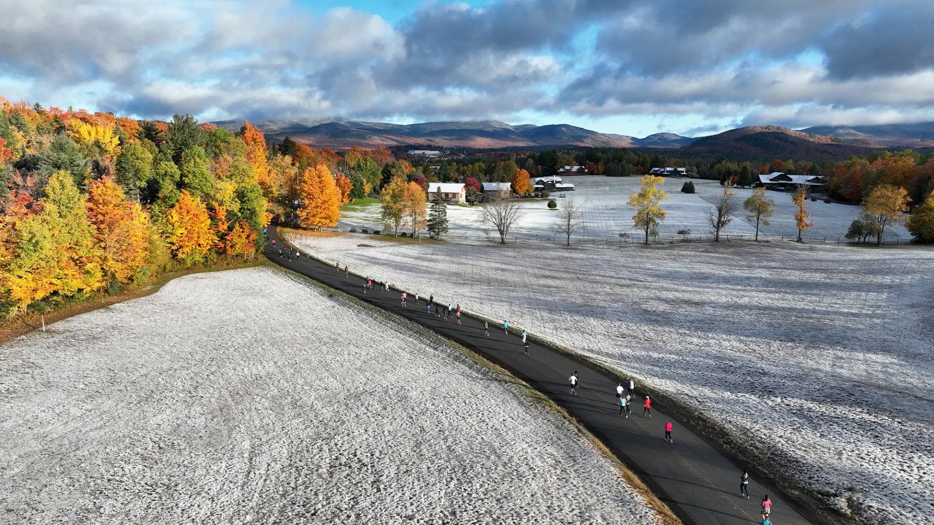 An aerial view of runners for the Lake Placid 10k running down a snow, fall foliage path.