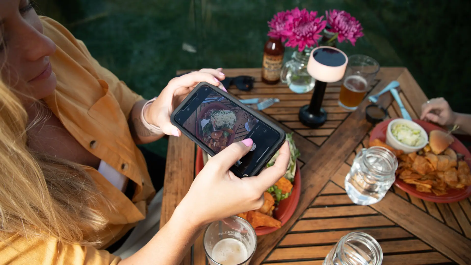 Looking down on a woman taking a photo of food on a restaurant table.