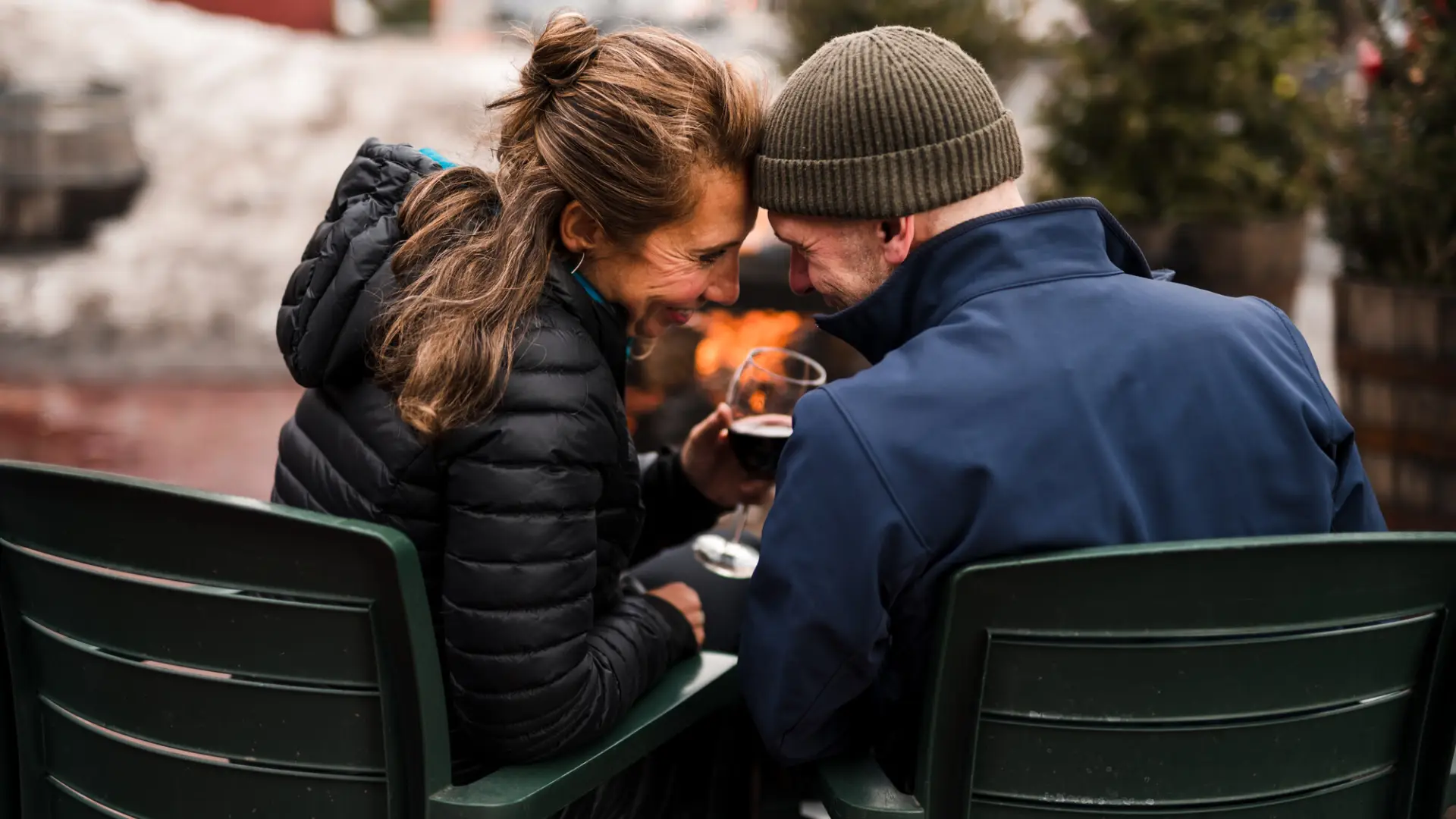 A man and woman share wine in Adirondack chairs.