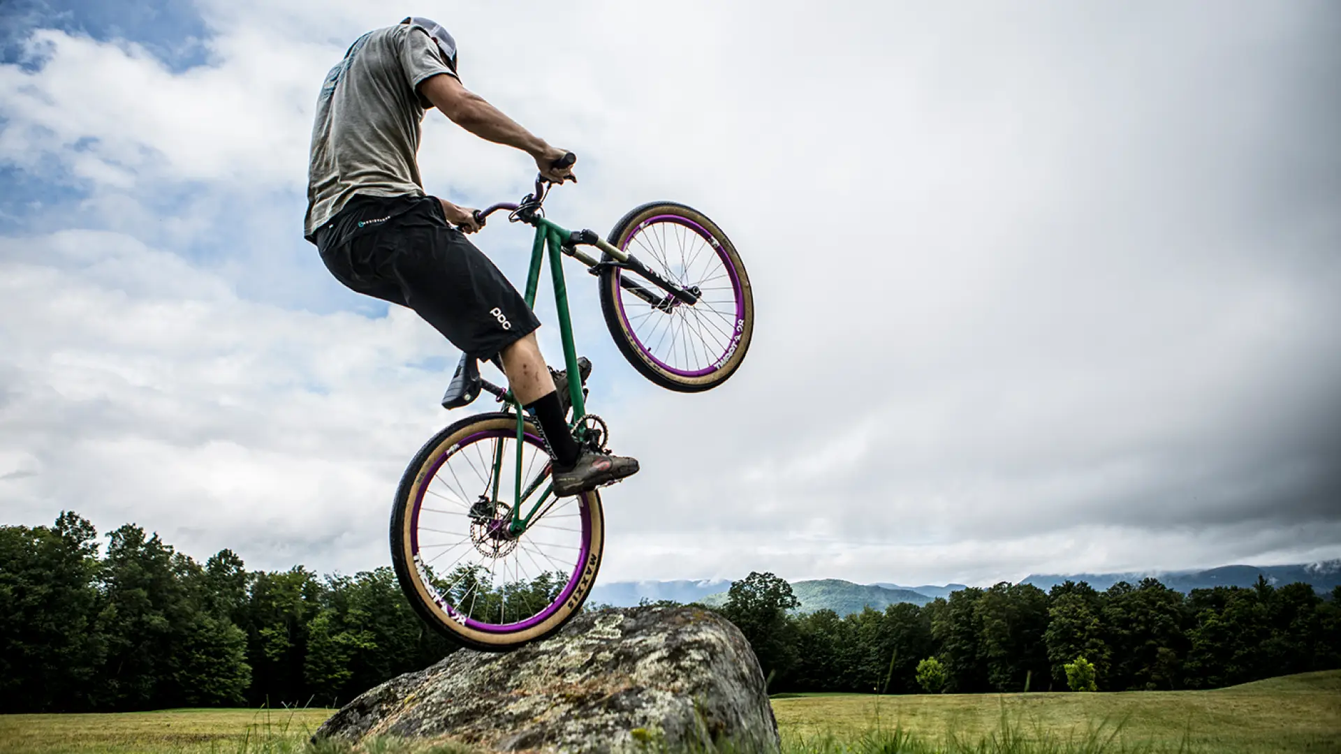 mountain biker pops up on their back wheel on a rock in a field at the Craig Wood Trails