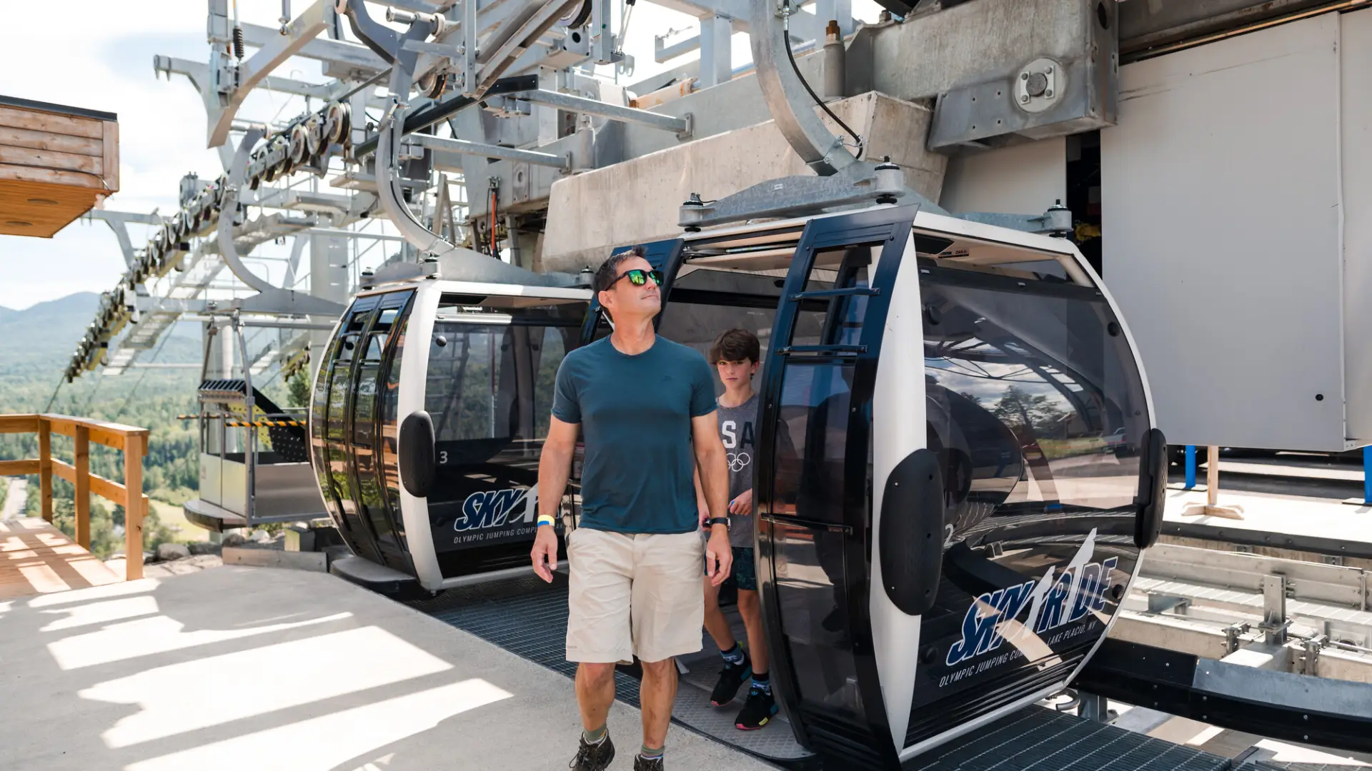 Man steps out of gondola looking around wearing t-shirt, shorts, and sunglasses