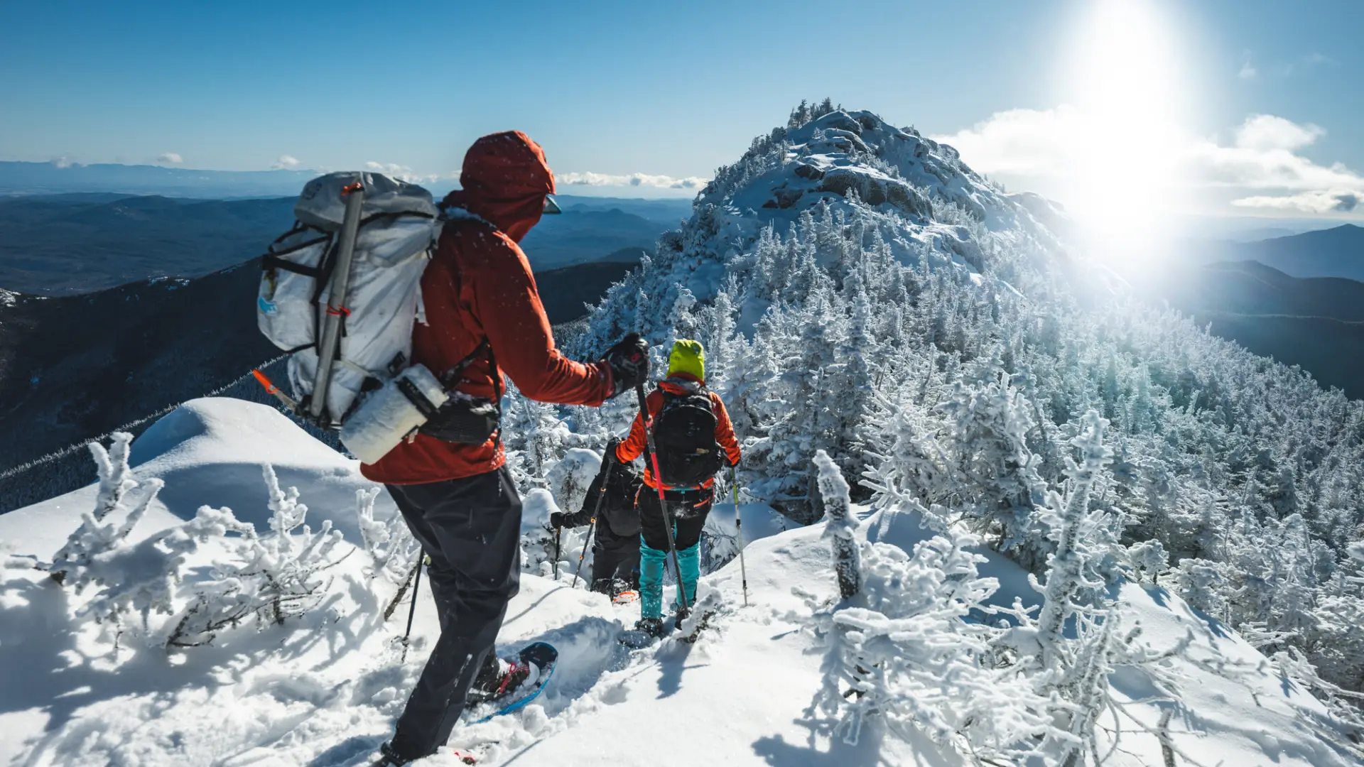 Three hikers descend a snow-covered mountain summit on a sunny winter day.