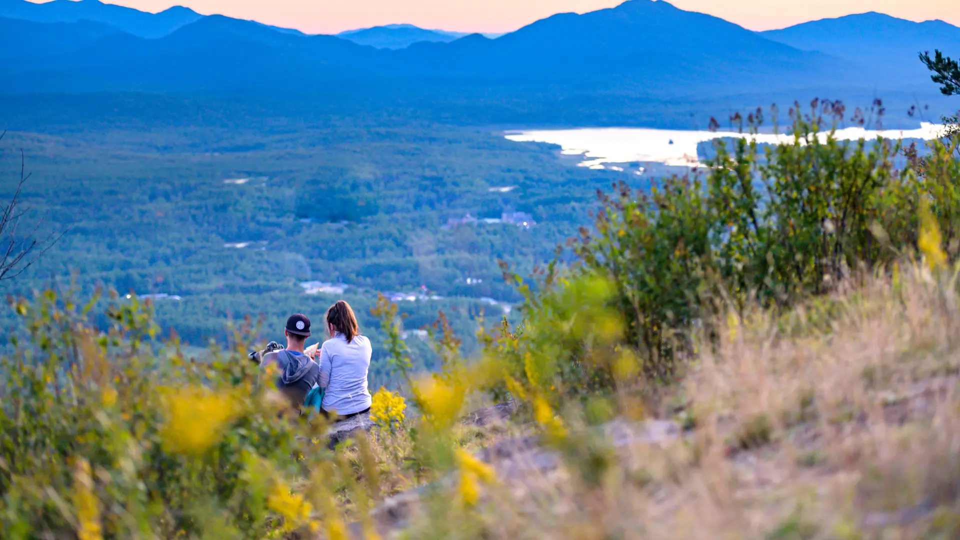 Two people look over at a view of mountains and a lake