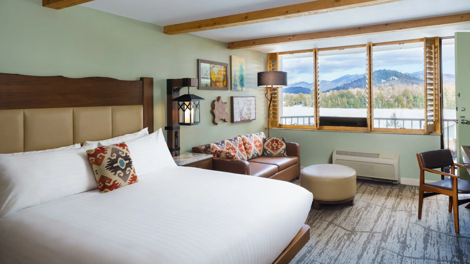 Large bed in hotel room next to leather couch with ottoman and winter lake view out the window