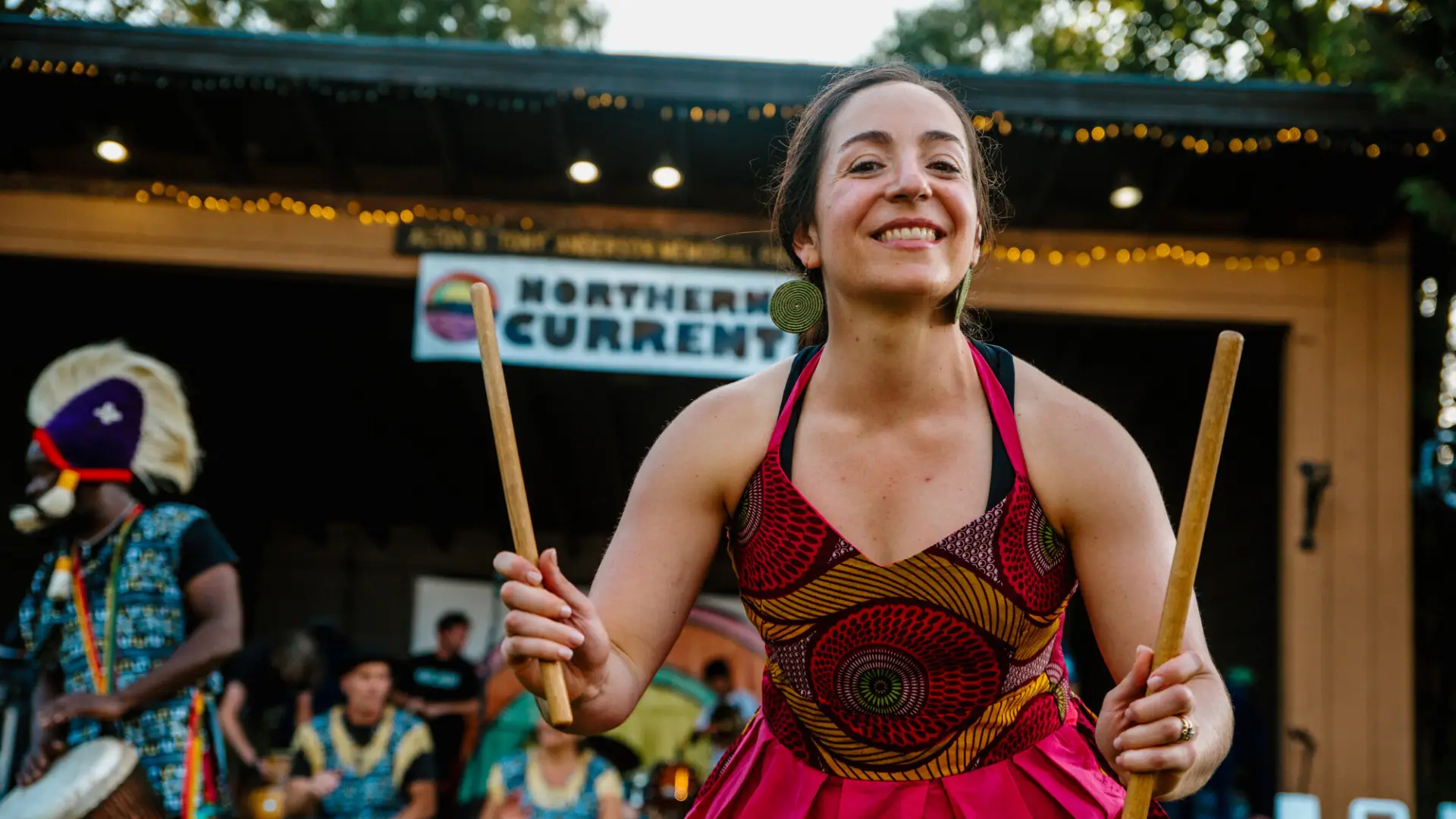 A friendly drummer in a colorful dress smiles into the crowd