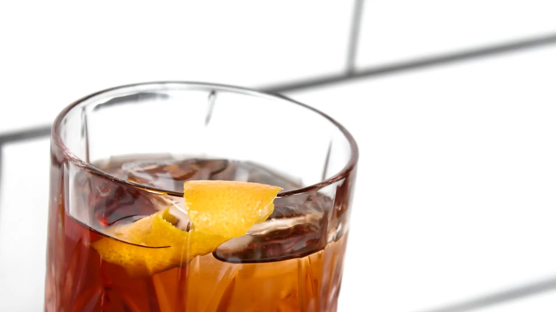Negroni cocktail in a cut low ball glass with a citrus peel garnish among fern leaves