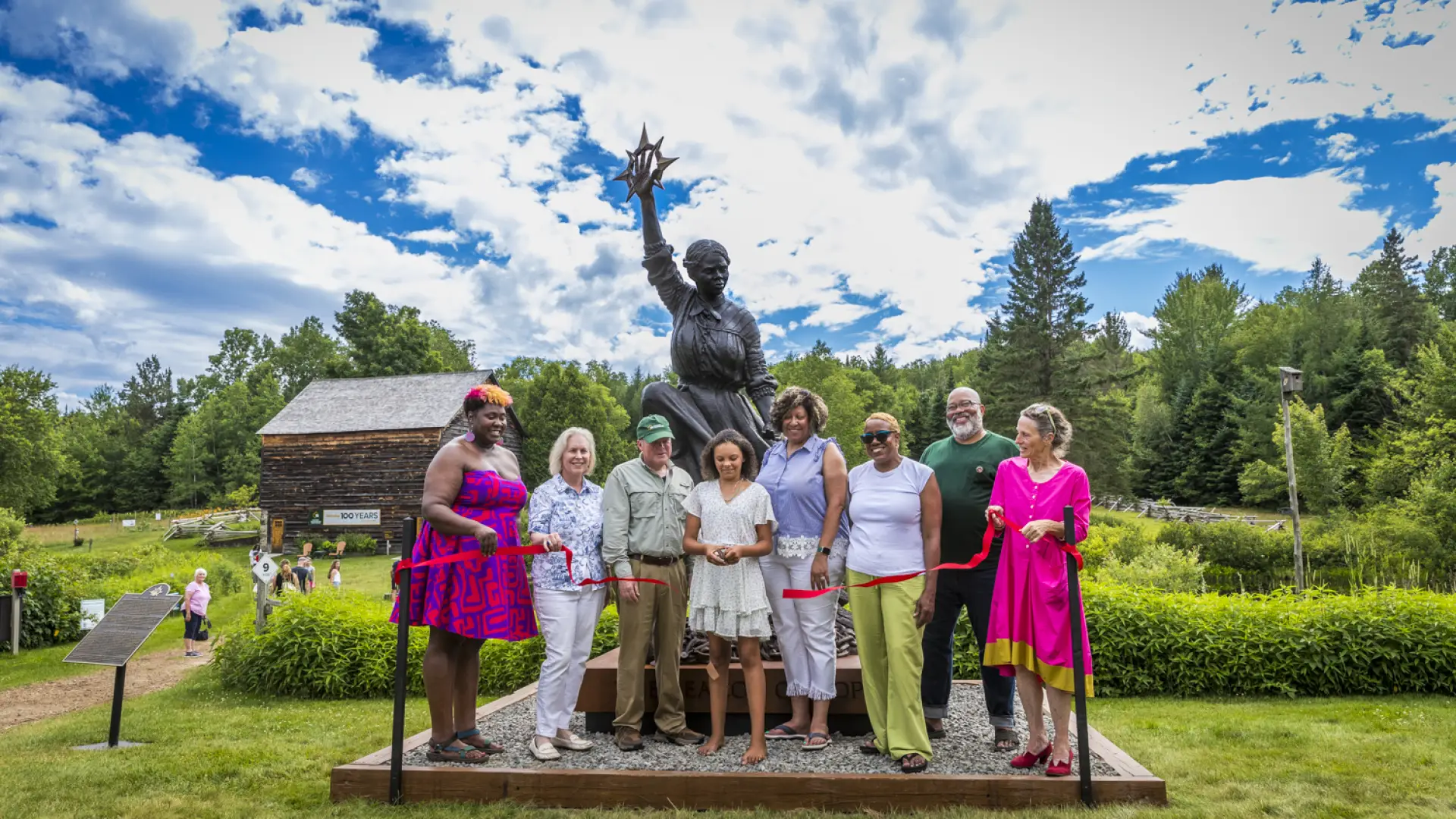 A group of people cut the ribbon on a new Harriet Tubman statue at John Brown Farm.