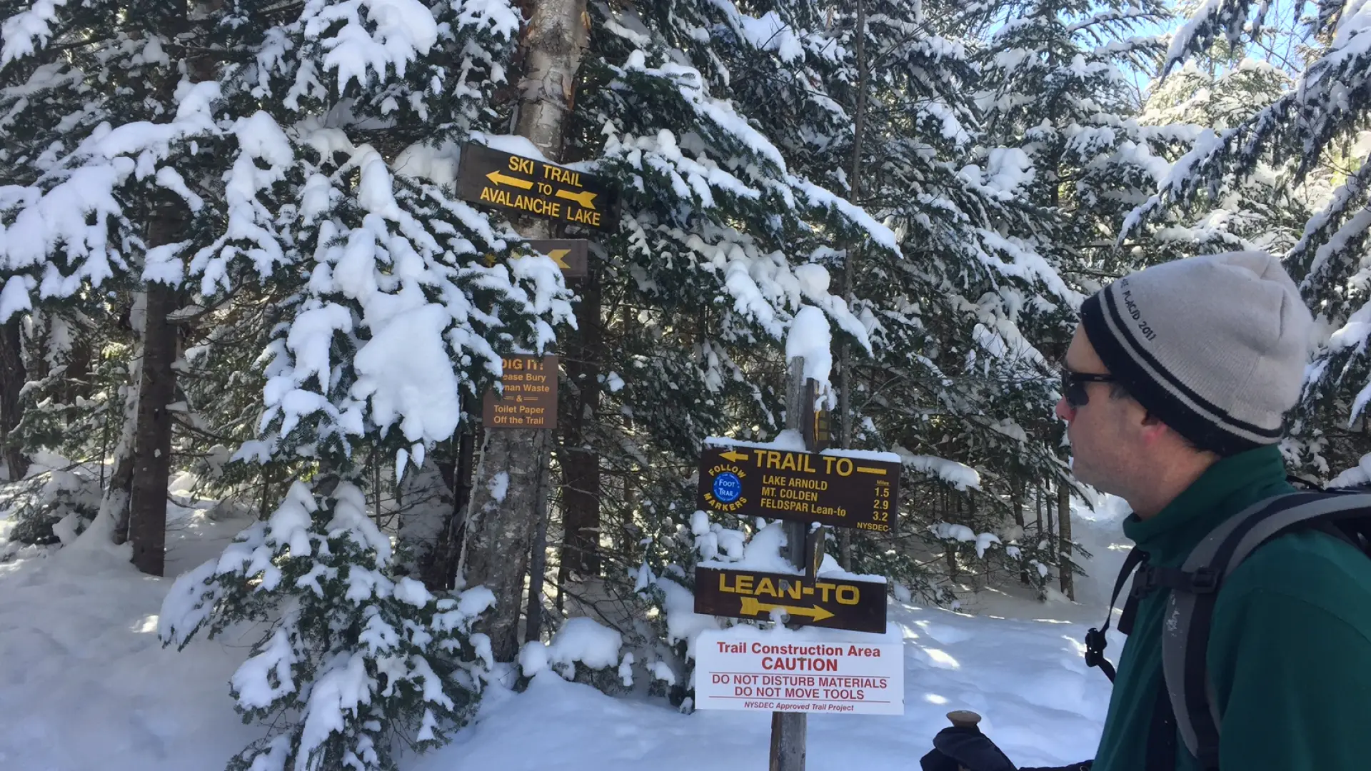 A hiker looking at wooden trail signs in the winter