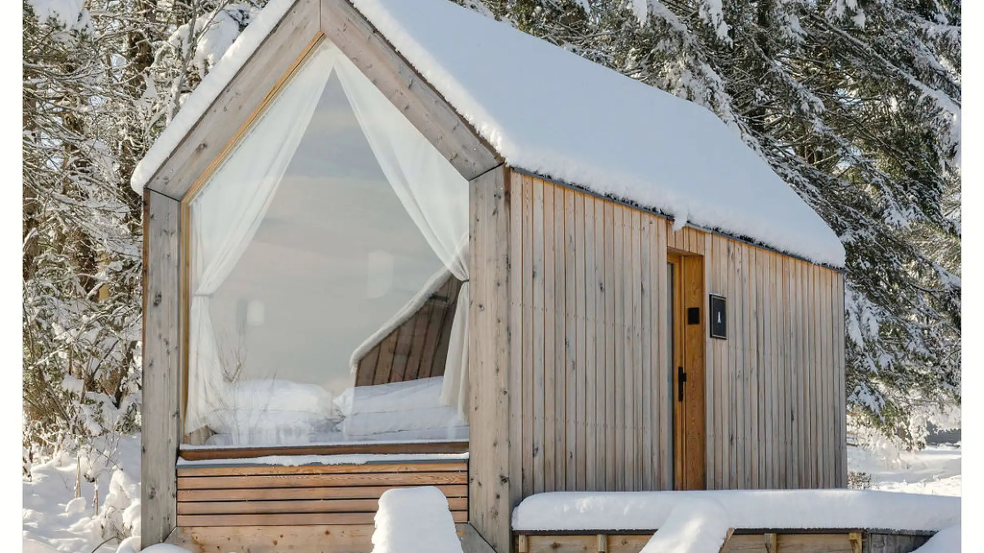 A minimum cabin blanketed in snow surrounded by tall pines