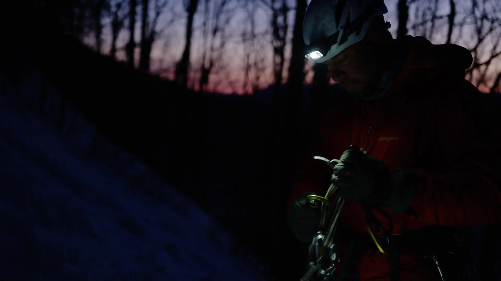 Man stands organizing ice climbing gear at dawn
