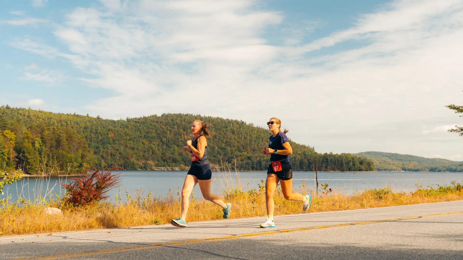 Two women run along a paved road during the Adirondack Marathon.