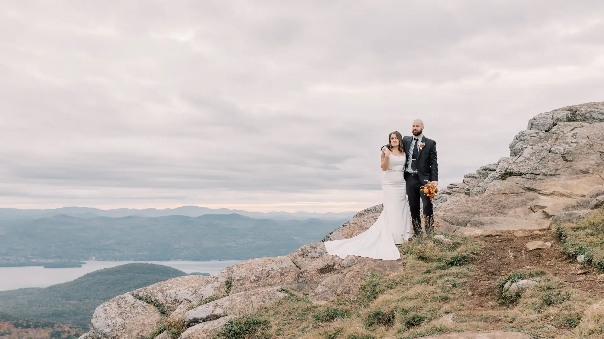 Bride and groom side hug on a rocky face overlooking the water