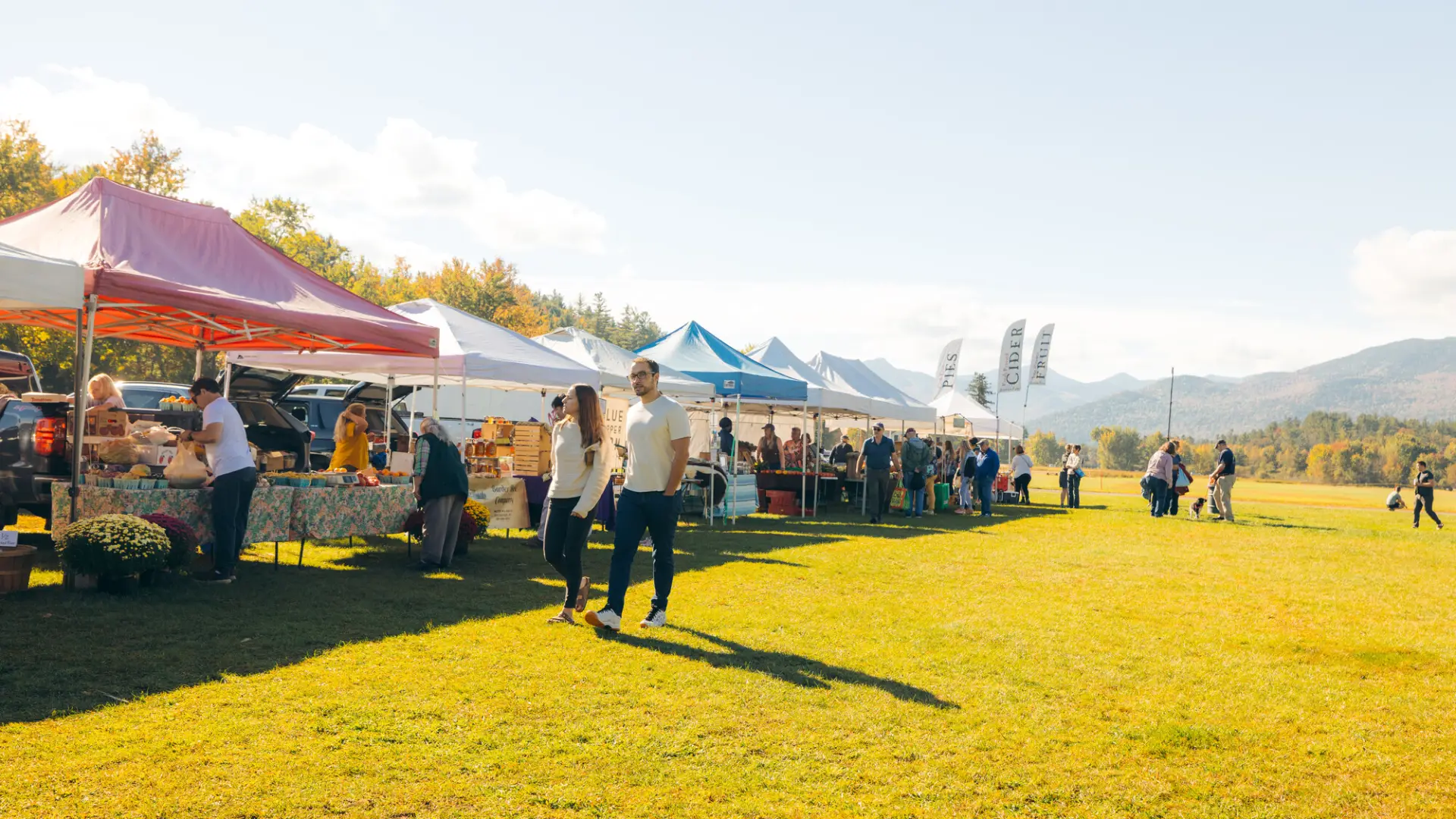 Couple holding hands walks past row of farmers market tents